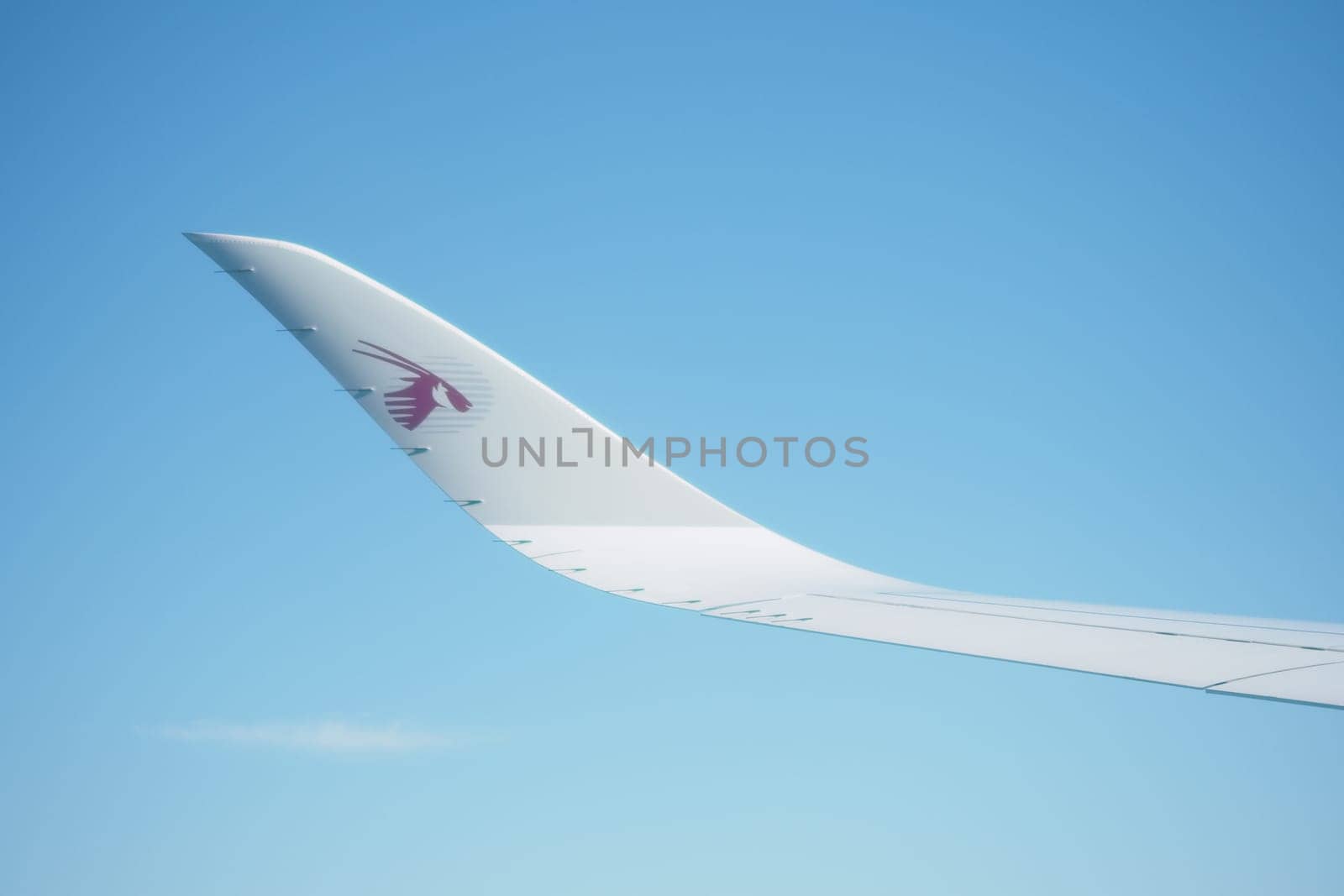 A close-up of an airplane wing gliding in the sky under sunlight.