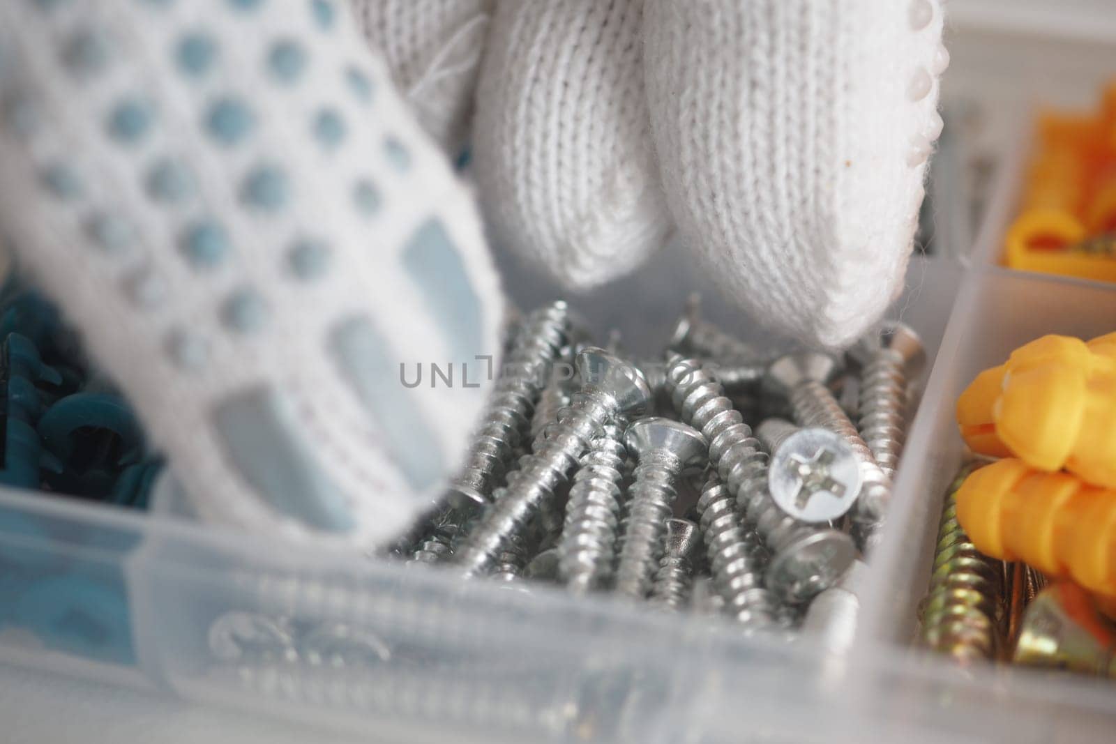 Gloved hands sort various screws in a storage container at a workshop.