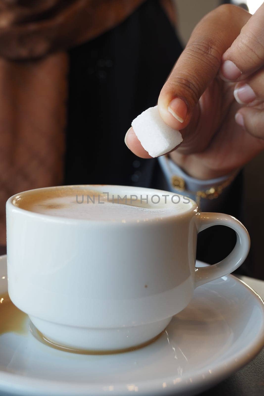 A person carefully places a sugar cube into a steaming cup of coffee.