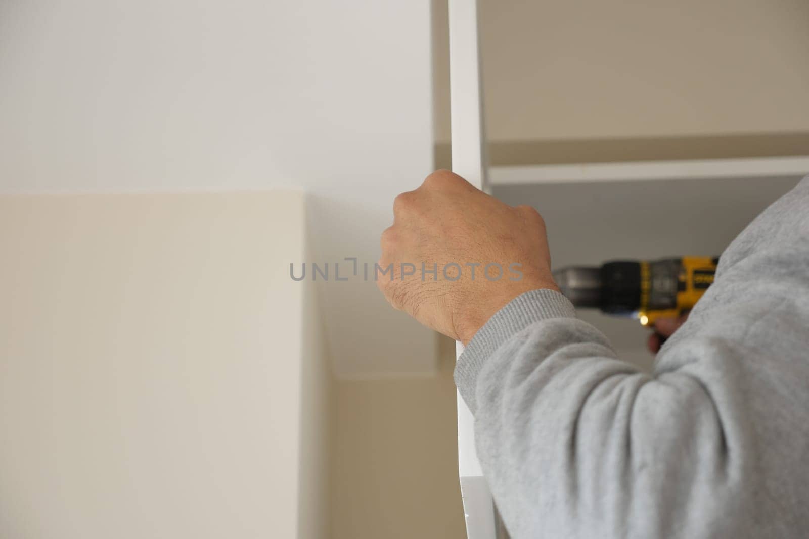 Hand of a person working on furniture assembly in a light room.