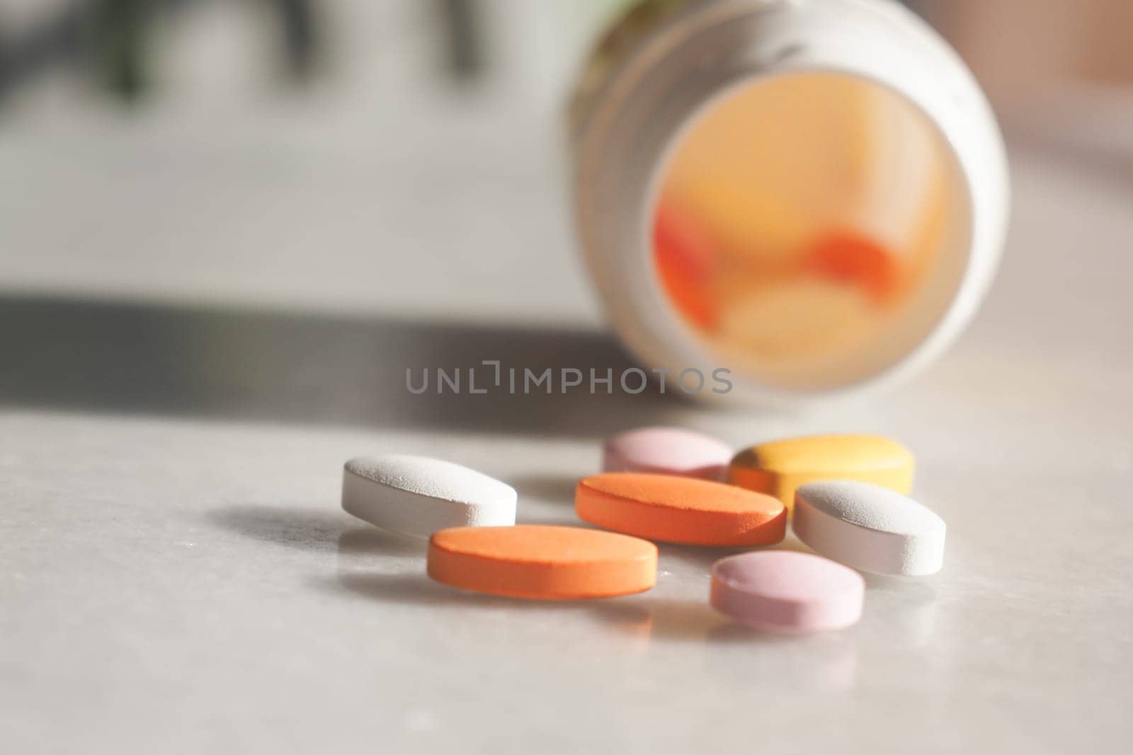 Various shaped tablets scatter on a surface near a prescription bottle.