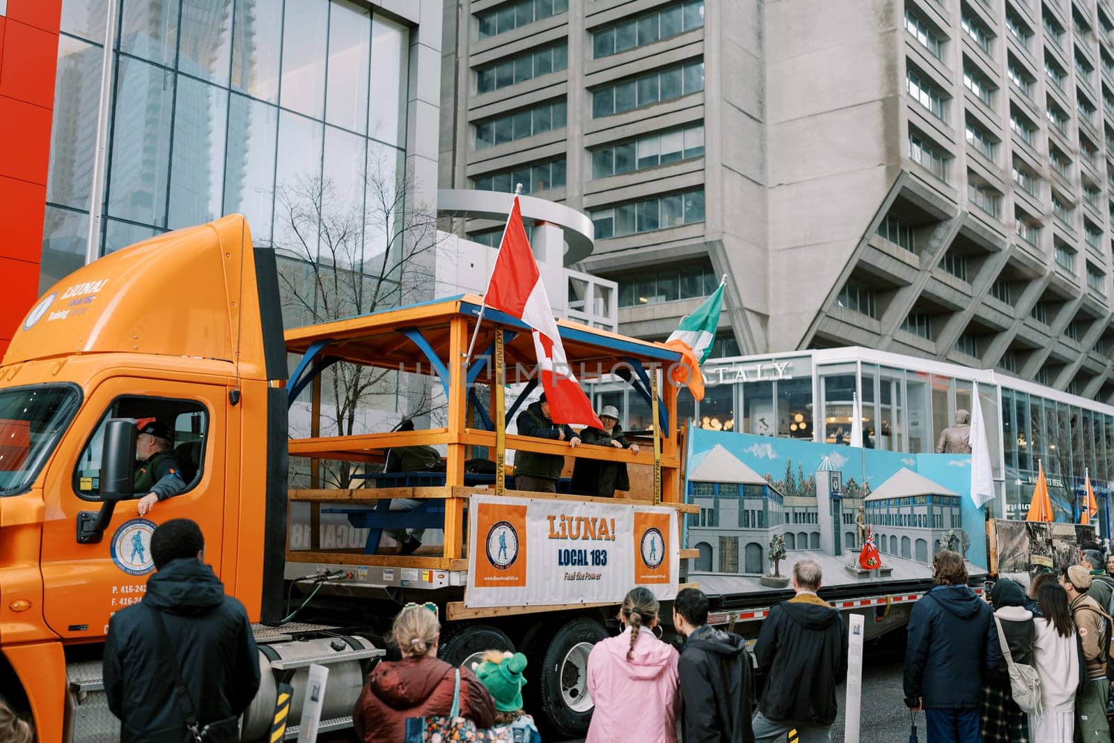 A vibrant parade with a decorated truck and a diverse crowd in the city
