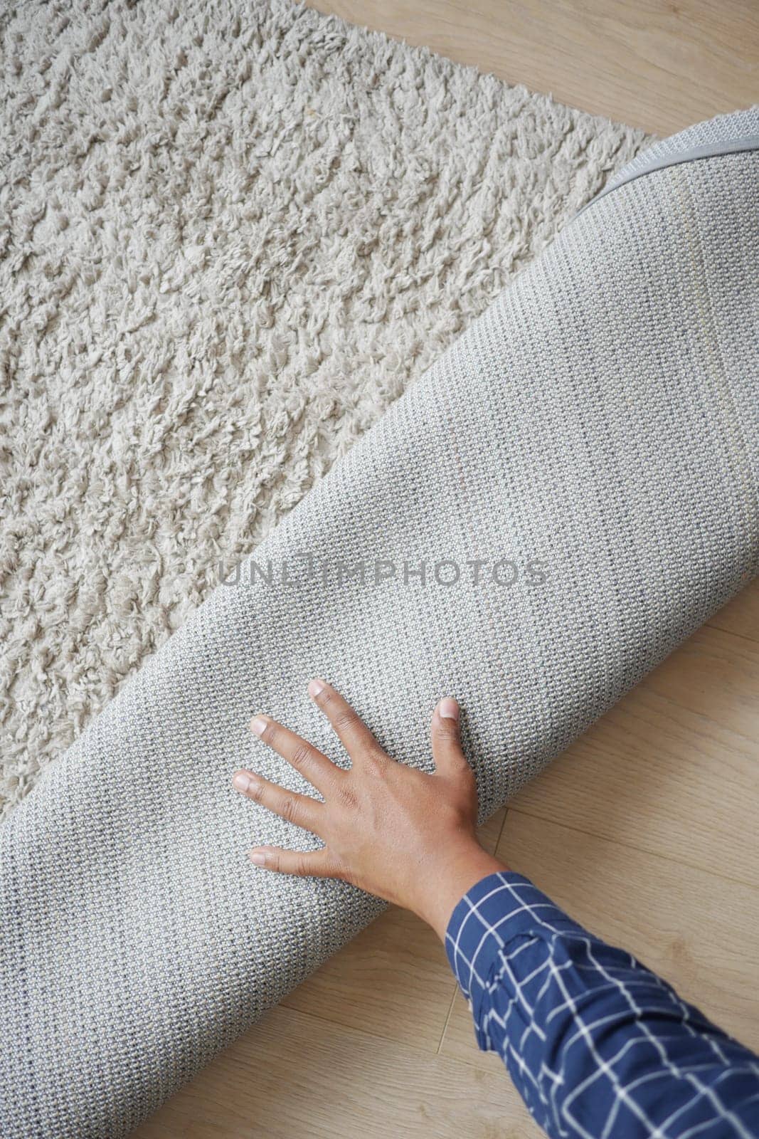 A hand is seen rolling up a gray rug on a wooden floor.