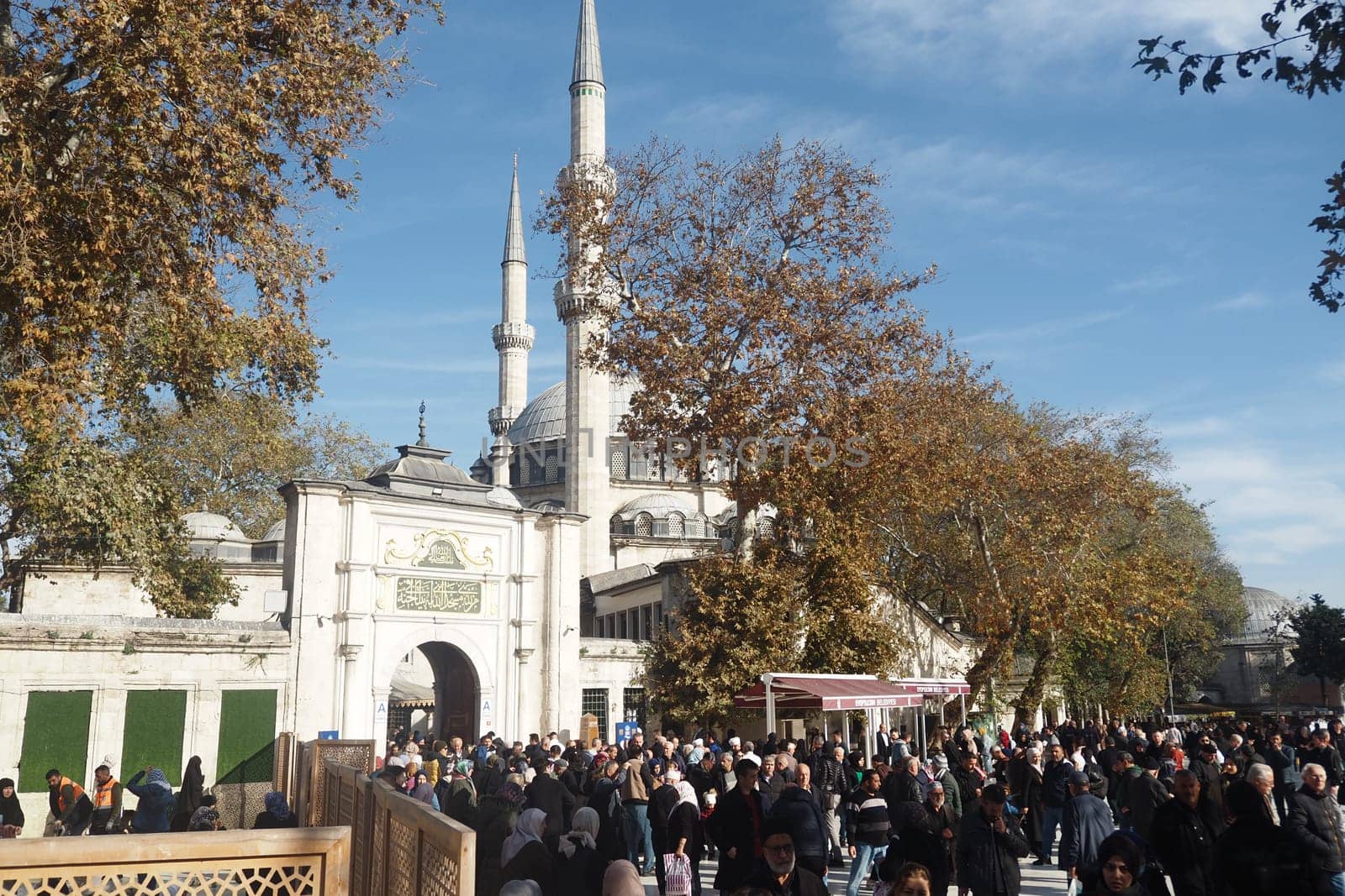 Crowds gather outside the mosque entrance on a sunny autumn day.