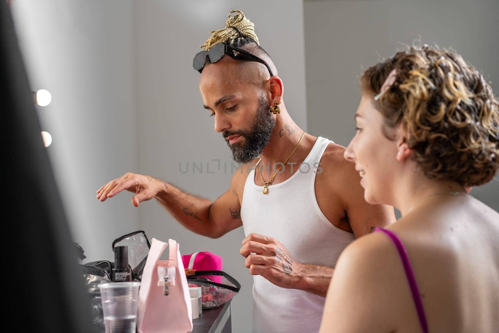 Professional male makeup artist applying makeup on female model in studio. Woman preparing for photoshoot, with makeup artist enhancing her look for the session
