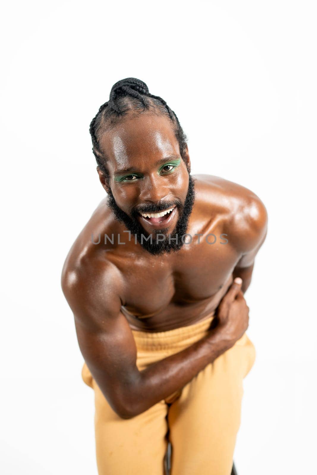Happy African American shirtless gay model bending over white background. Portrait of cheerful homosexual man posing in plain studio
