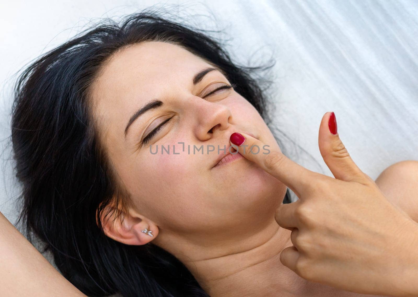 A young woman lounges comfortably in a hammock, basking in the warm sunlight. She seems lost in thought, playfully touching her lips while enjoying a peaceful moment in nature.