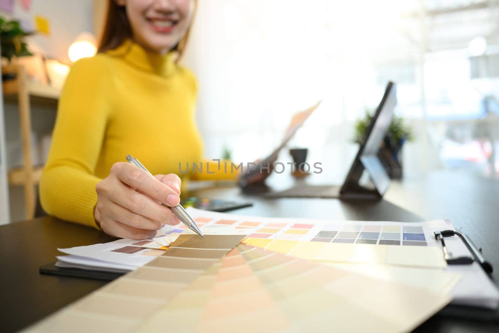 Smiling female designer choosing color samples for design project at graphic studio.