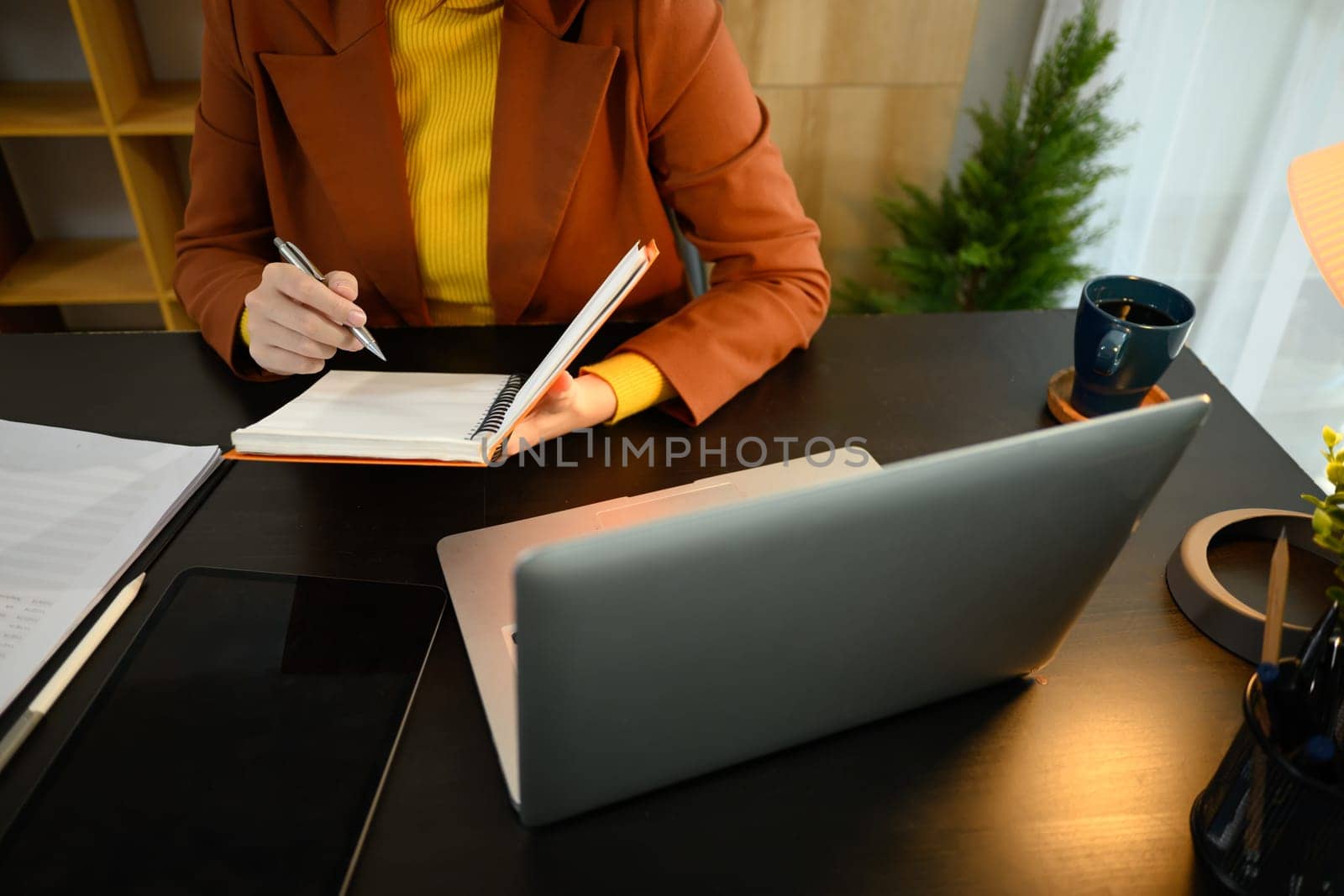 Focused entrepreneur planning and writing ideas on a notebook, sitting in a bright workspace.