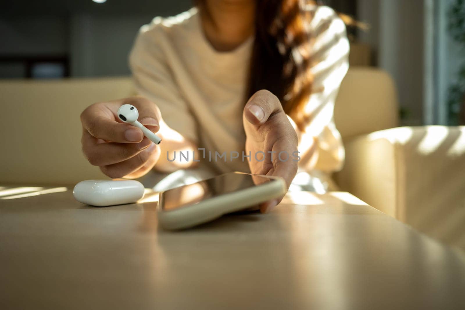 Young woman holding a wireless earbud and reaching for her smartphone.