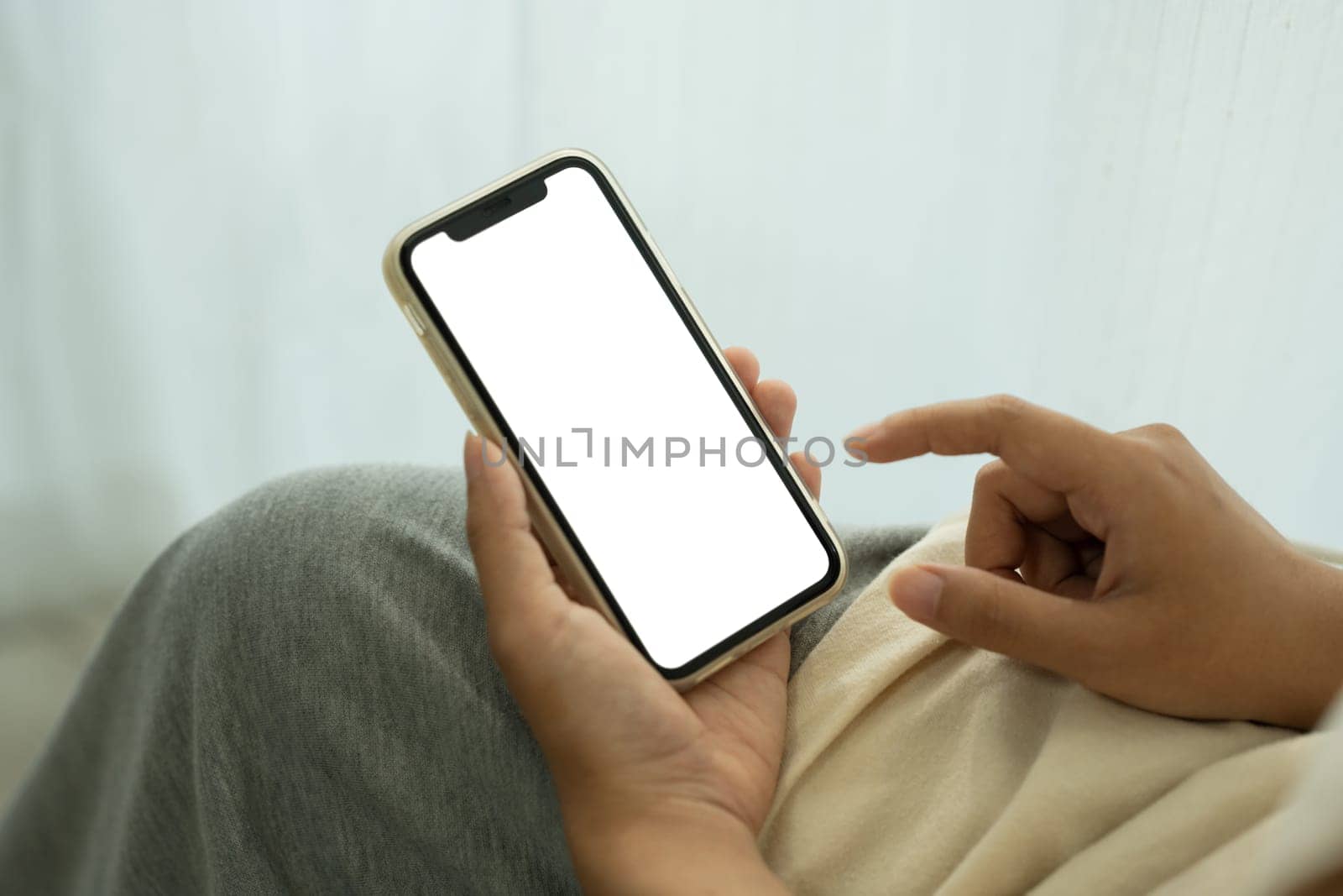 Close up of hands holding smartphone with a blank screen sitting near window with sheer curtains.