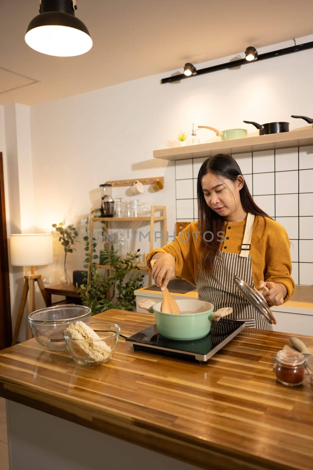 Happy asian woman in an apron stands in a kitchen, preparing a quick and easy meal.
