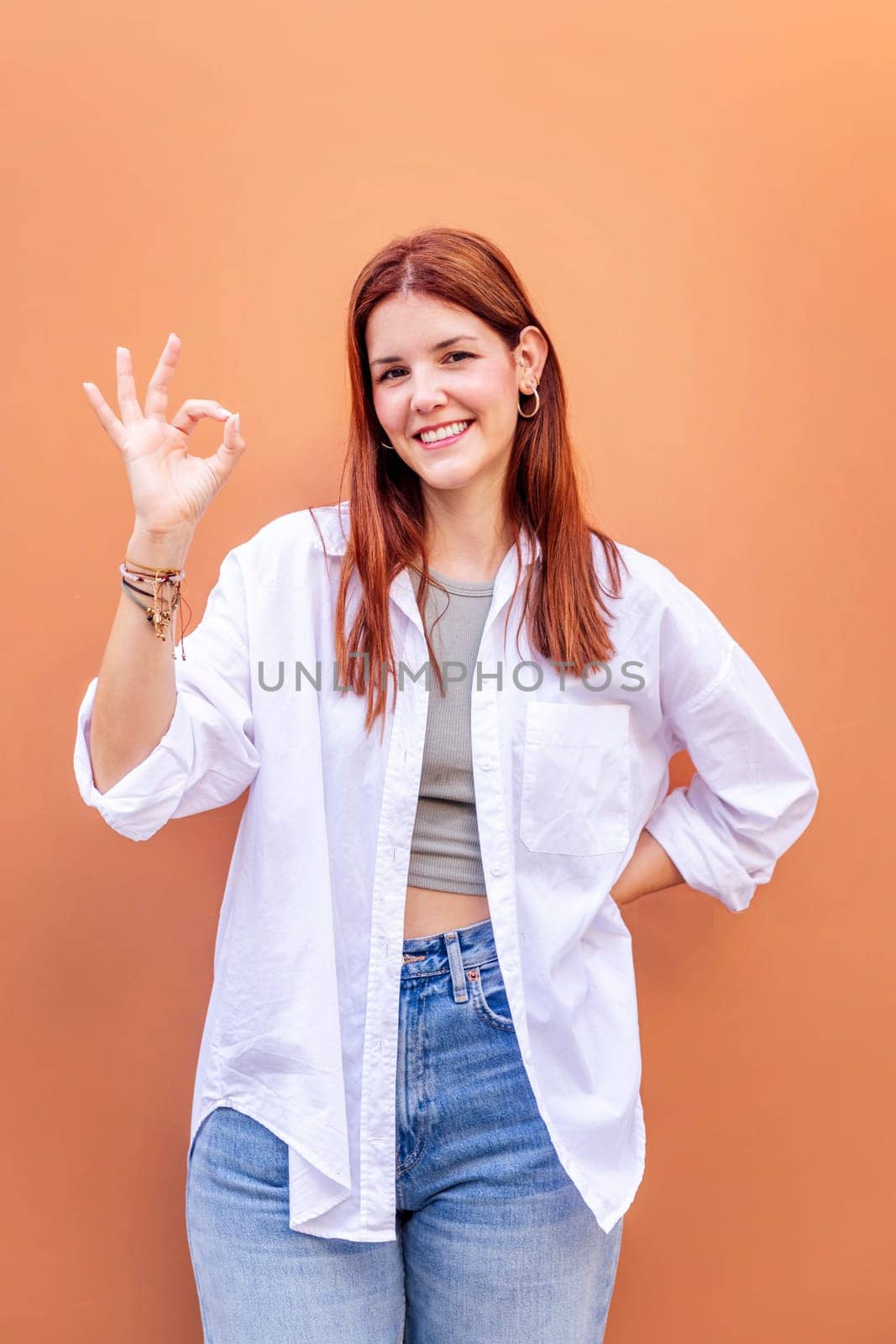 young woman doing ok sign with hand while smiling looking at camera in a positive and friendly mood suggesting that she is happy and content, copyspace for text