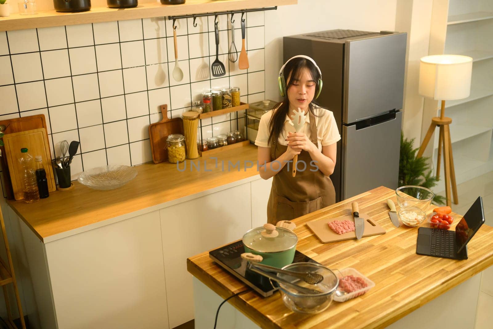 Happy young woman listening to music with headphones and enjoys cooking in a cozy kitchen.