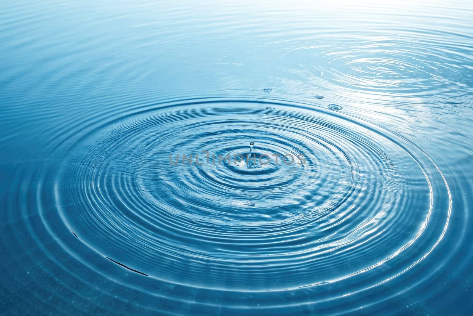 Gentle ripples spread across a calm blue lake as a droplet falls, creating a mesmerizing pattern. The early dawn light casts a peaceful glow, enhancing the beauty of this natural moment.