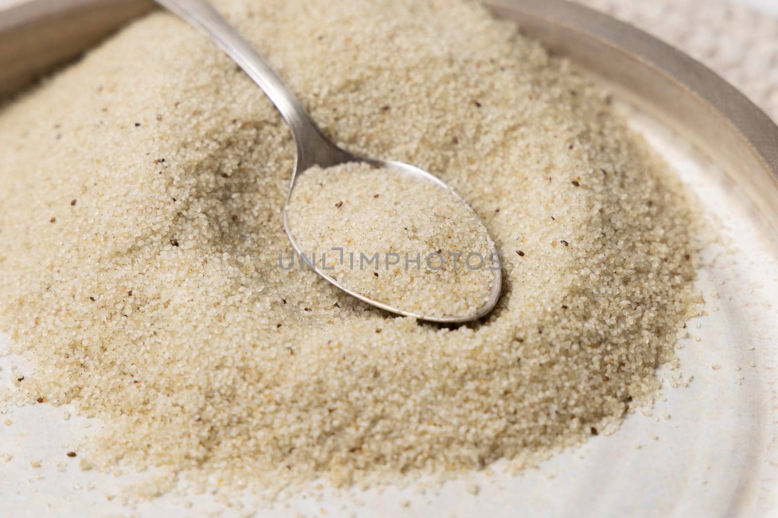 Plate ofraw uncooked fonio seeds with a metal spoon on white table close up. African ancient pseudocereal. Organic super food. Healthy food concept. Gluten free alternative seeds