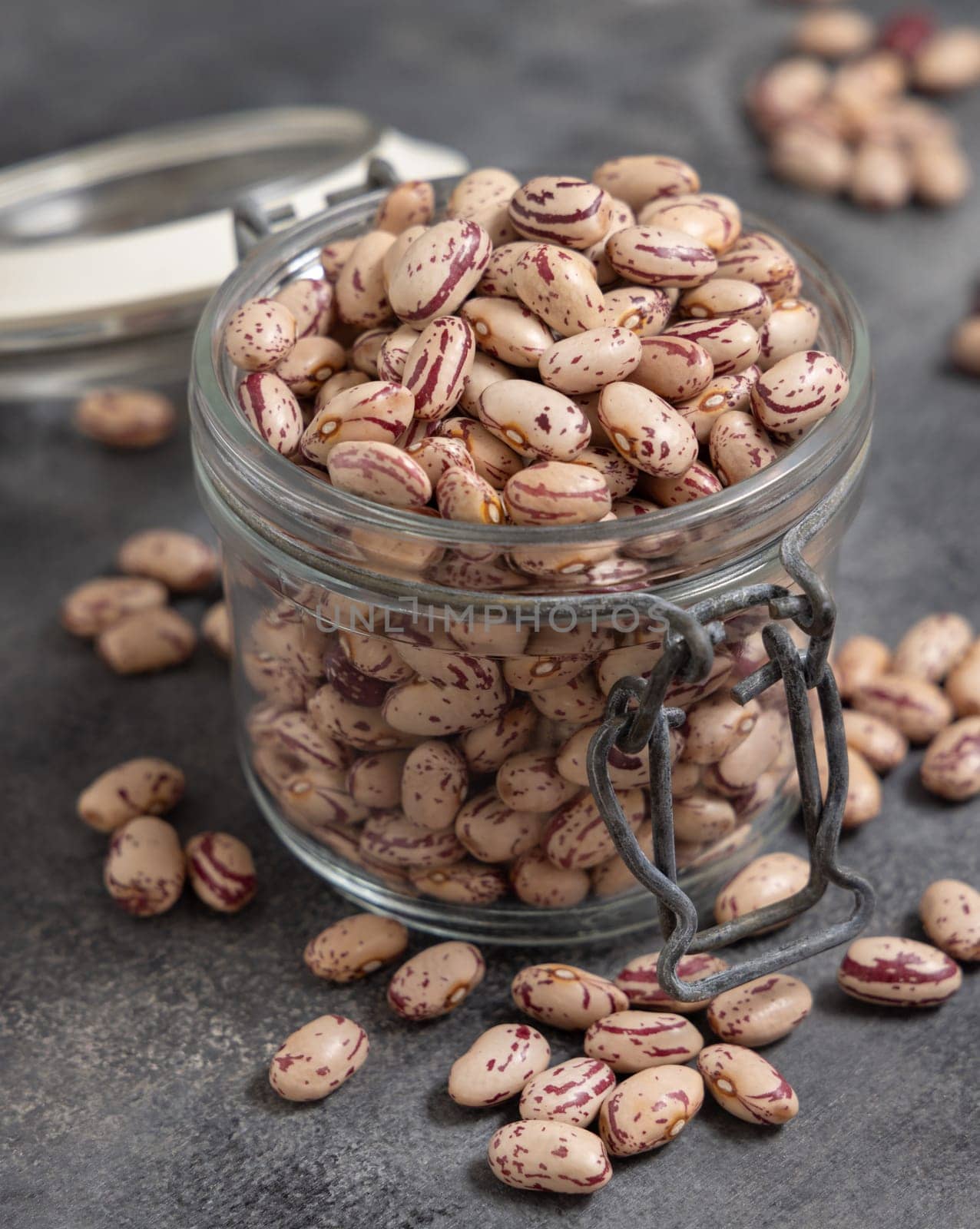 Opened glass jar full of dried pinto beans on gray table closeup. Healthy vegetarian food, legumes protein source. Traditional Latin American cousin ingredient