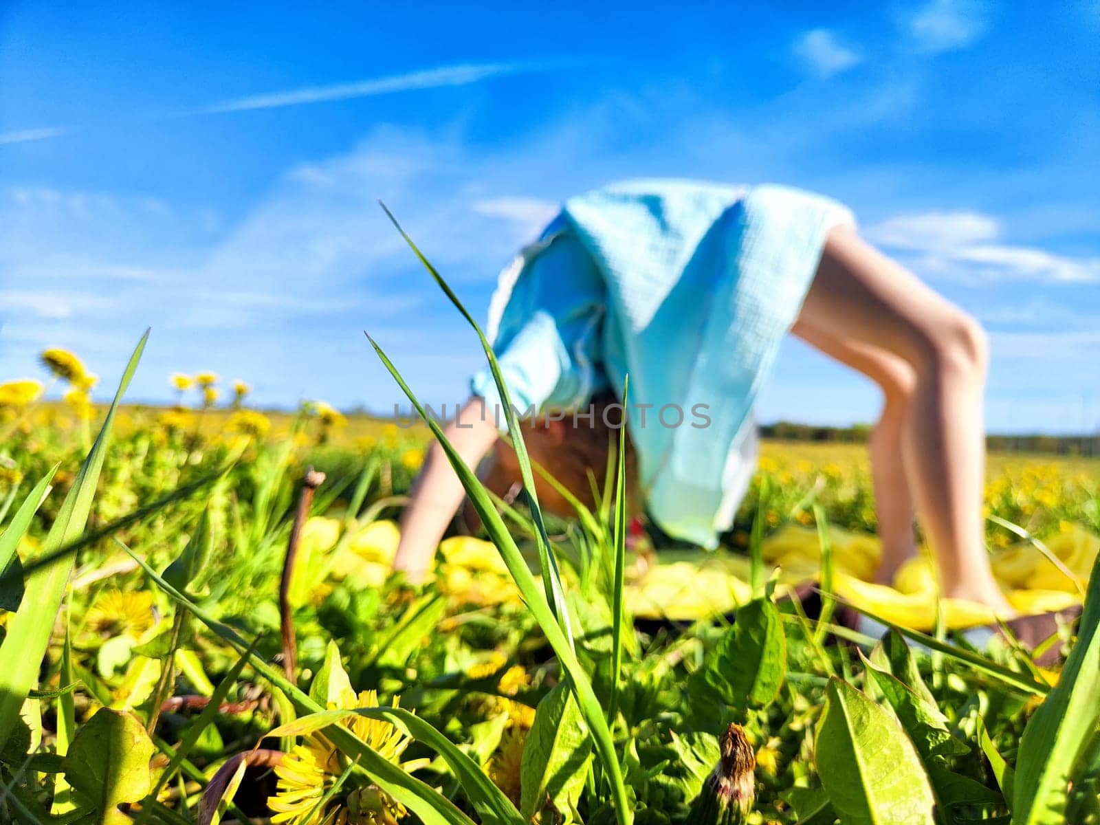 A joyful child balances upside down in a grassy field filled with blooming dandelions under a clear blue sky.