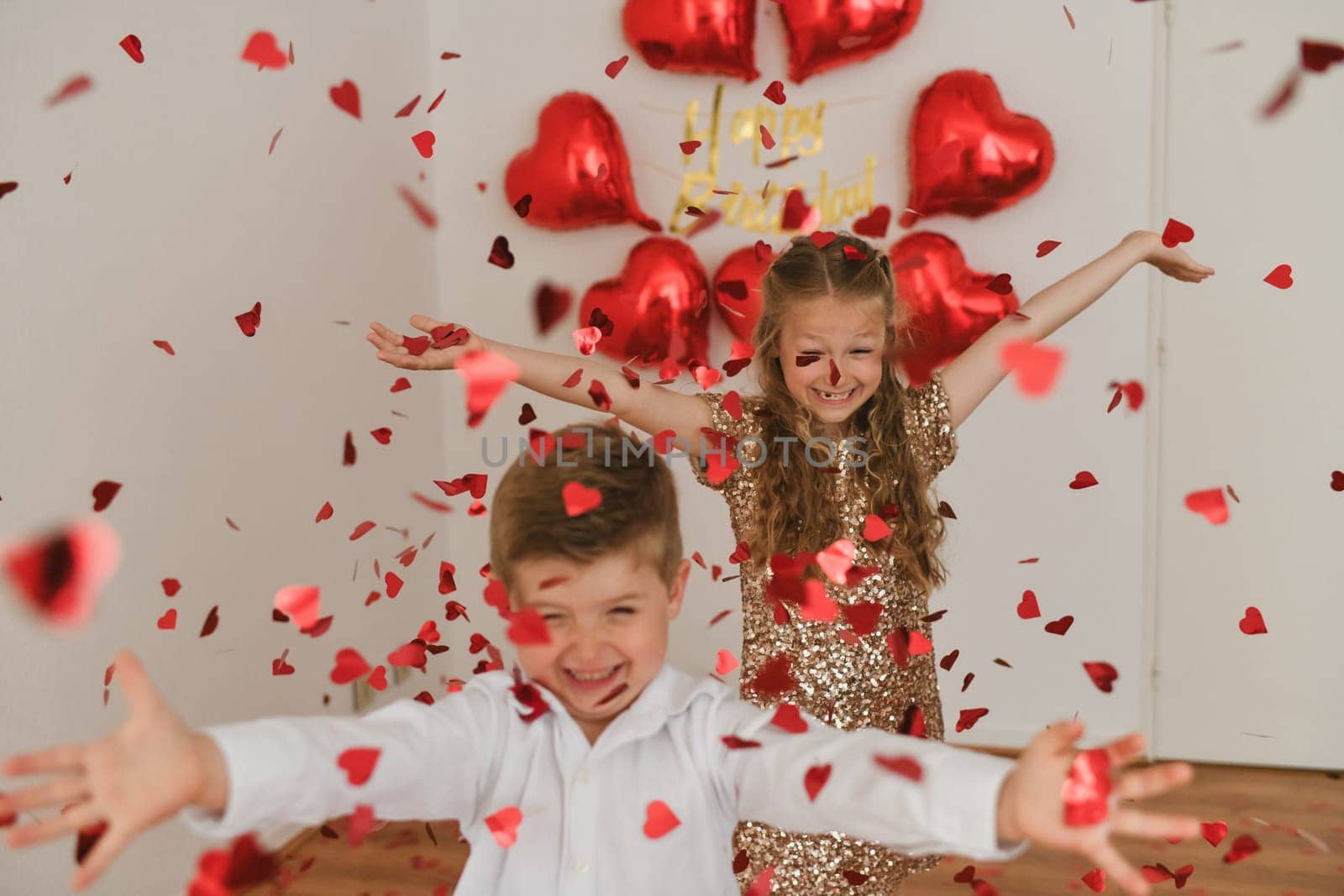 Children enjoy heart-shaped confetti. Balloons are in the background.Valentines Day concept