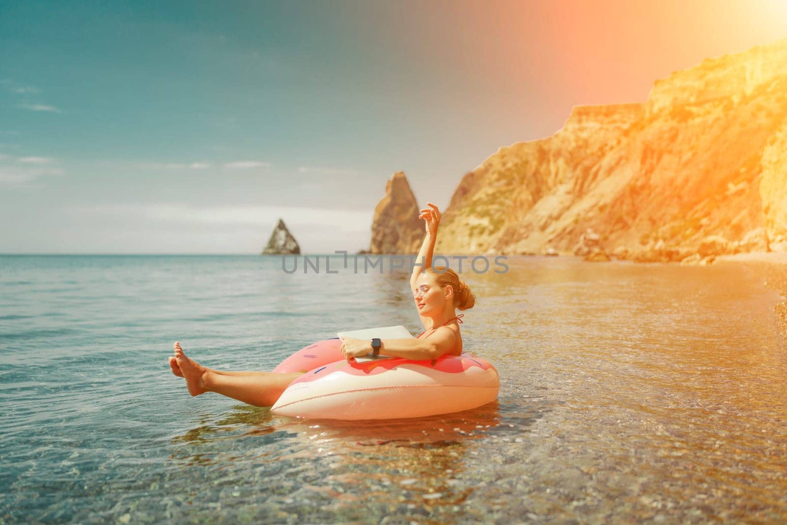 Woman laptop sea. Freelancer woman in sunglases floating on an inflatable big pink donut with a laptop in the sea. People summer vacation rest lifestyle concept