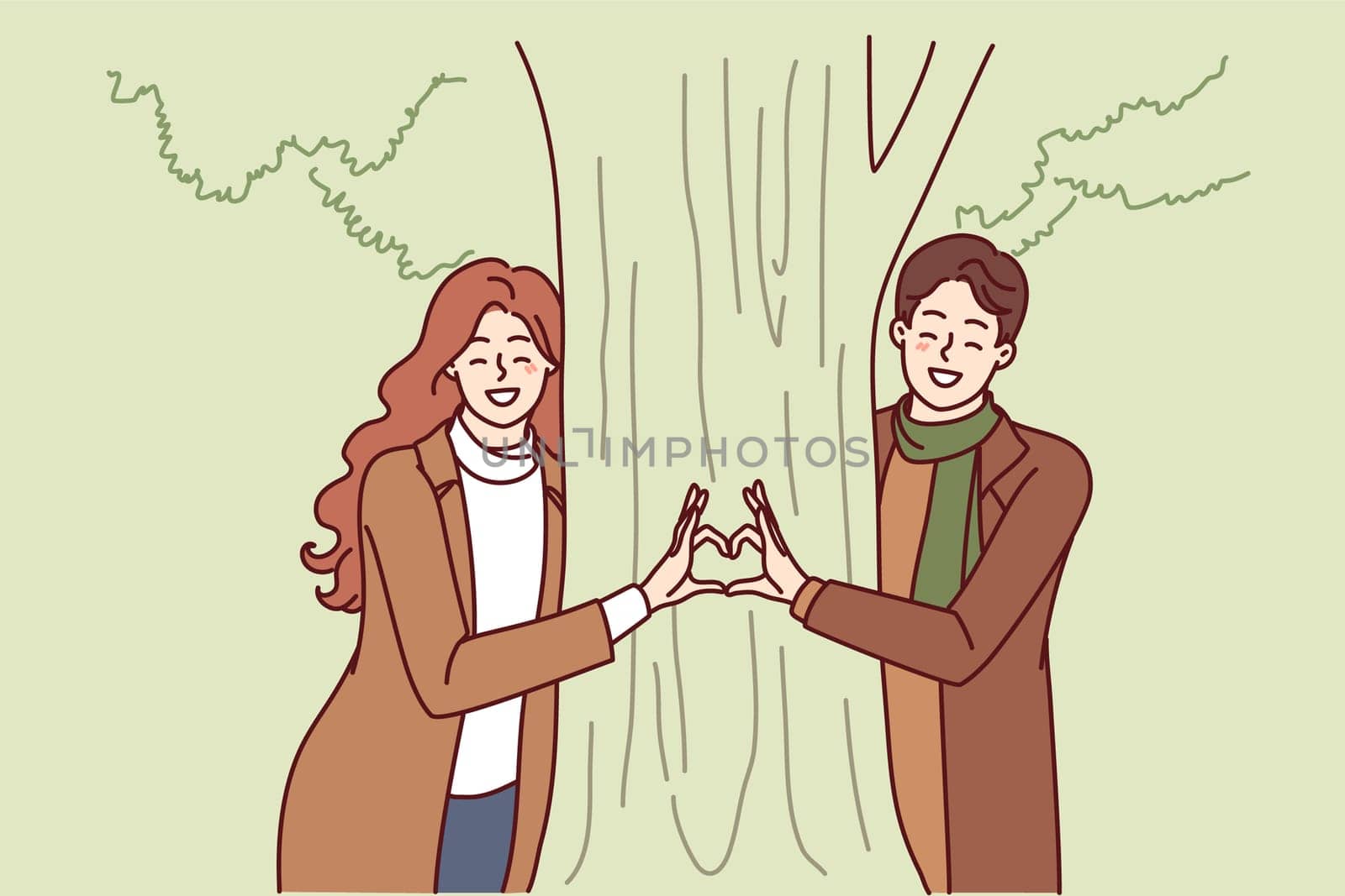 Happy couple stands near tree together making heart from their fingers as sign of love for partner and ecology. Man and woman are in love and spend date in park enjoying joint vacation