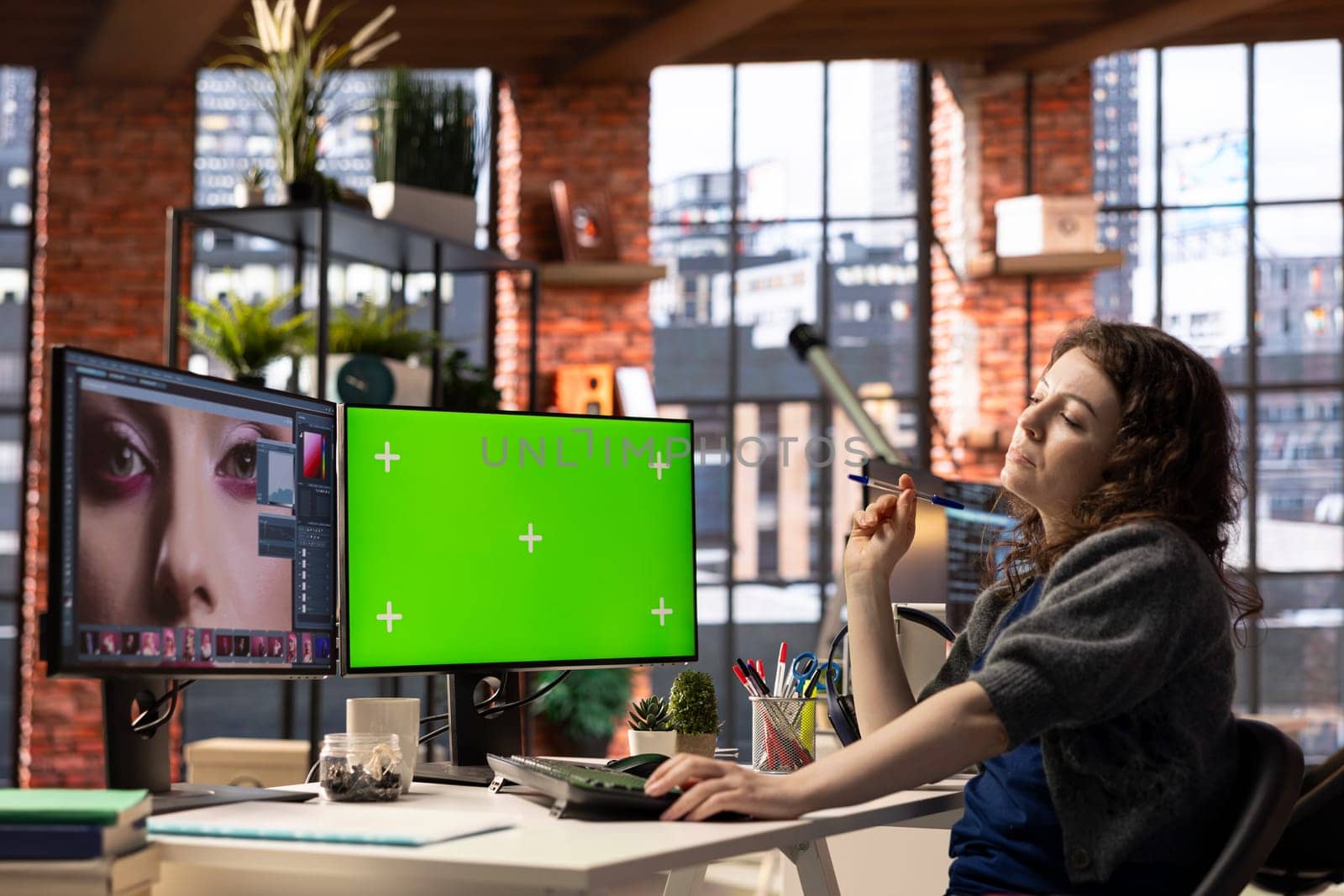 Female graphic designer uses editing software and green screen for photo retouching in a well organized workspace. Young editor expert uses digital tools essential for a creative artistic career.