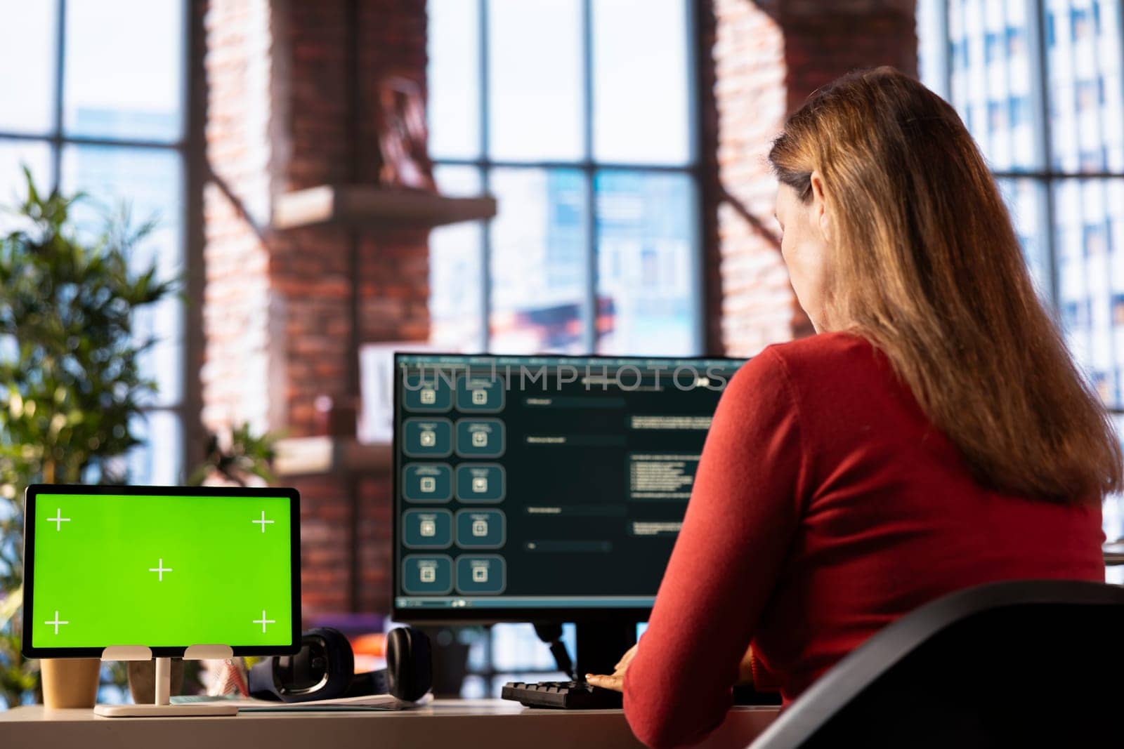 Mature woman engaging with AI chatbot on pc next to isolated display, using the virtual assistant with prompts for data driven algorithms to enhance productivity at home office.