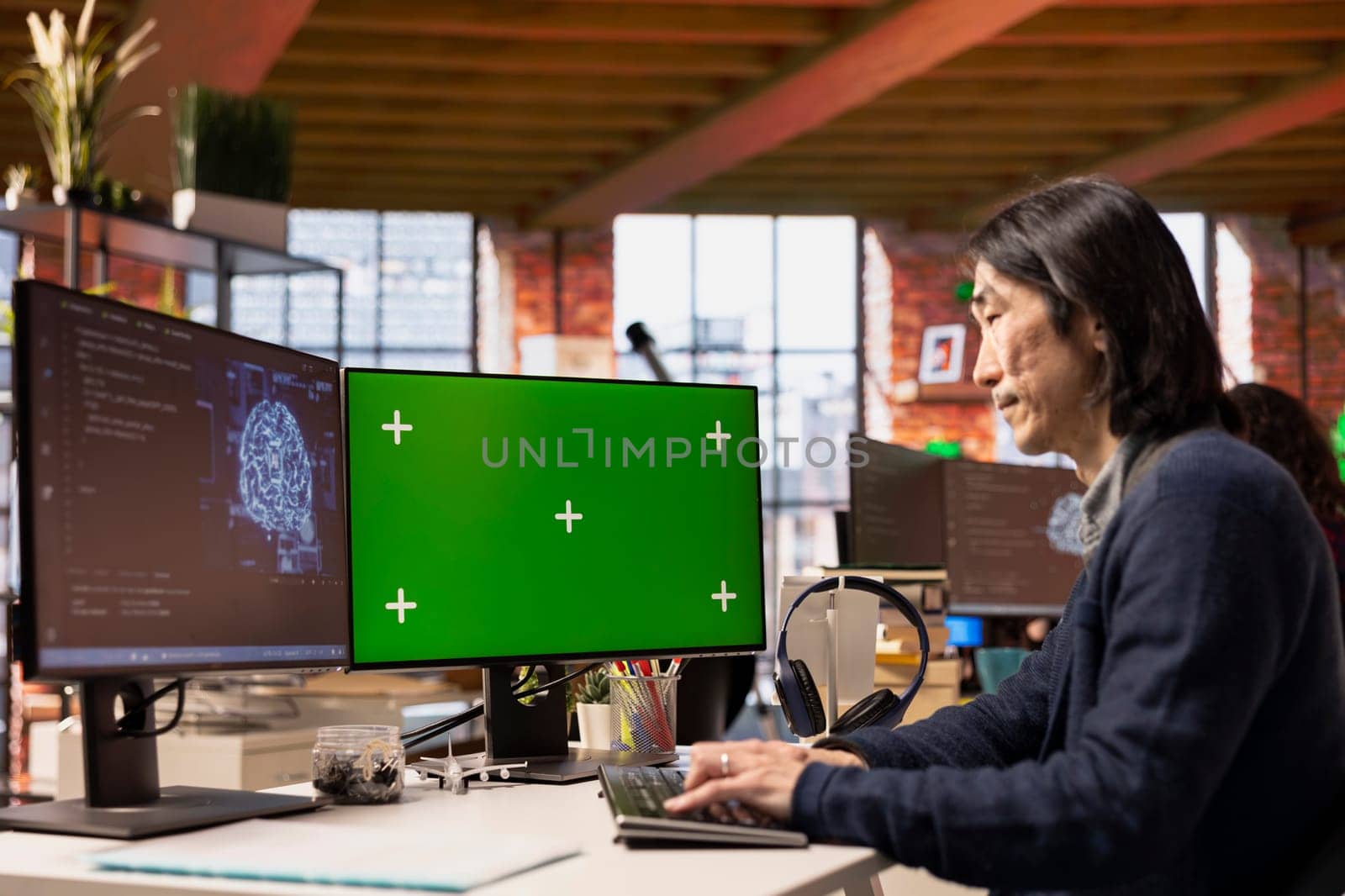 Software developer in pioneering technology startup using green screen computer to oversee artificial intelligence neural networks. Man in tech startup office using AI to build product on mockup PC