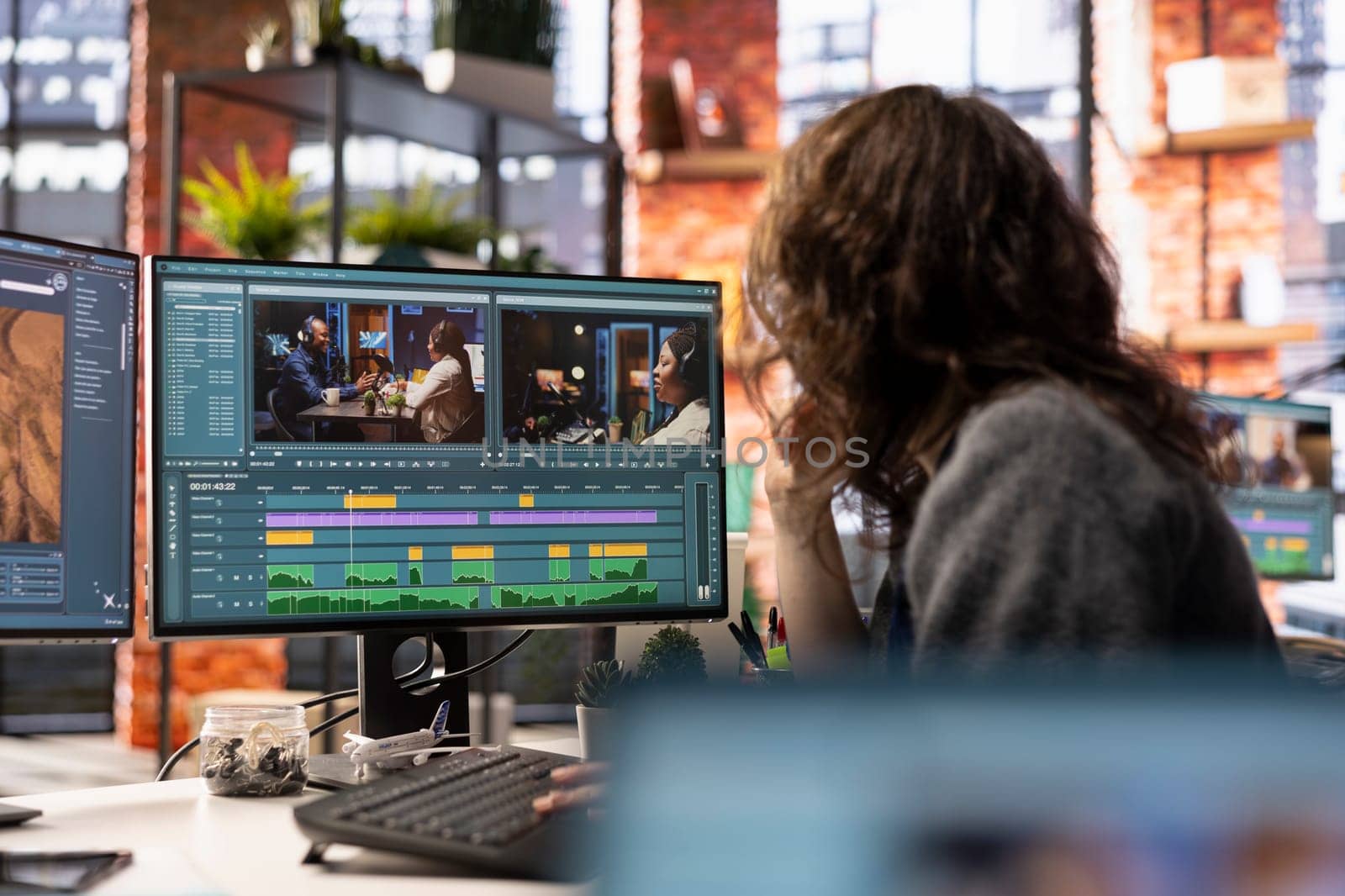 Video creator woman editing a music video on dual monitors in agency studio, multitasking between timeline editing and color grading. Professional editor uses tech tools and software.