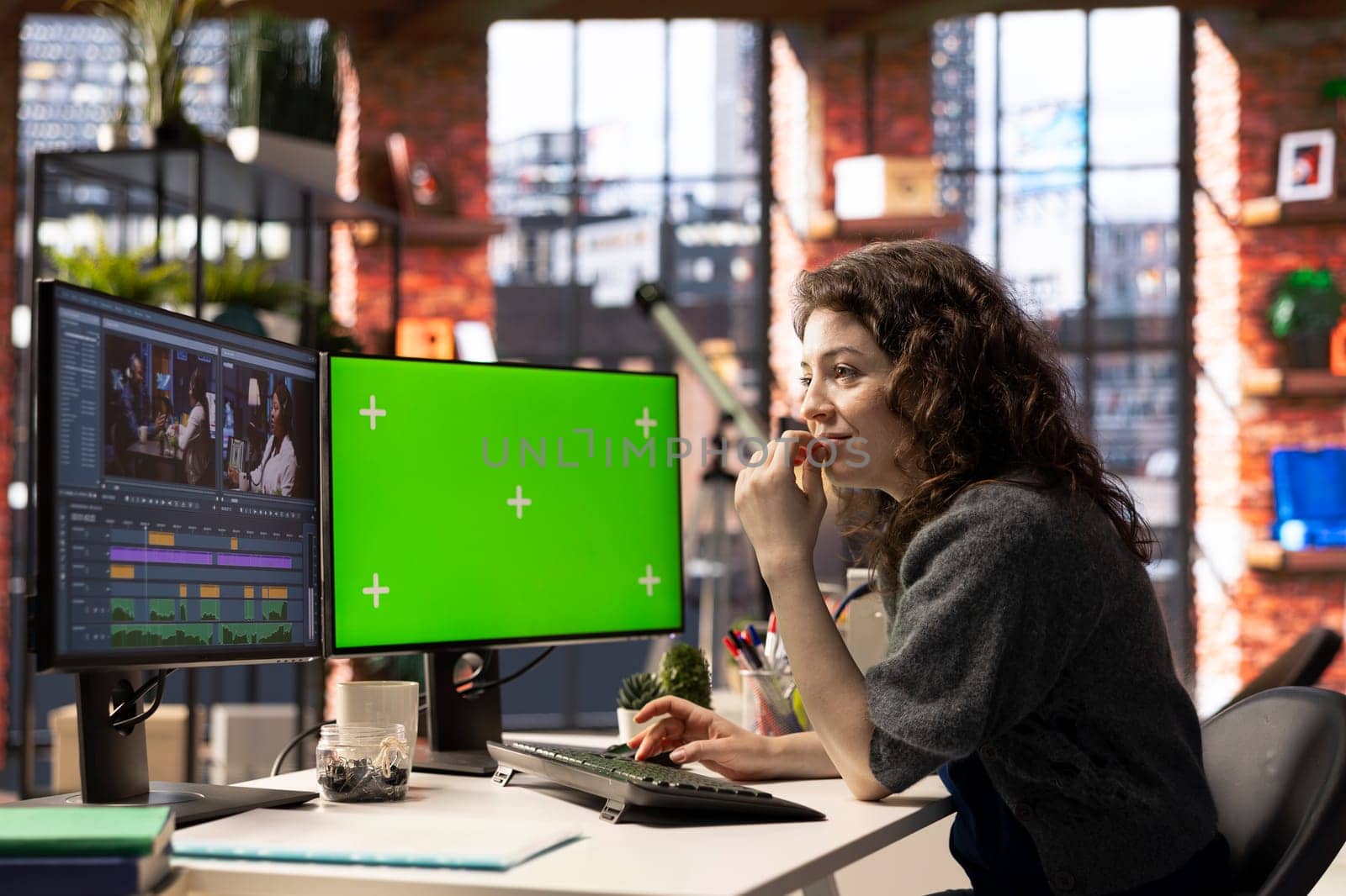 Woman video creator edits a multimedia project next to chroma key at agency office, using professional tech tools and editing software to manage timeline editing and video production.