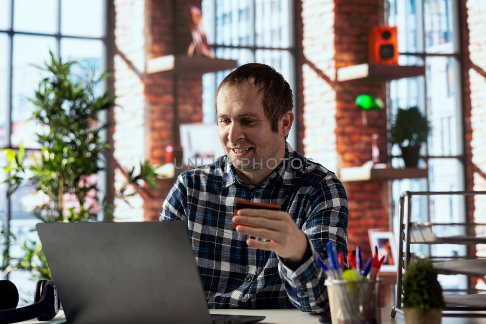 Happy man doing internet shopping, carefully typing credit card information on laptop in apartment. Cheerful shopper adding payment method on website while at home in living room
