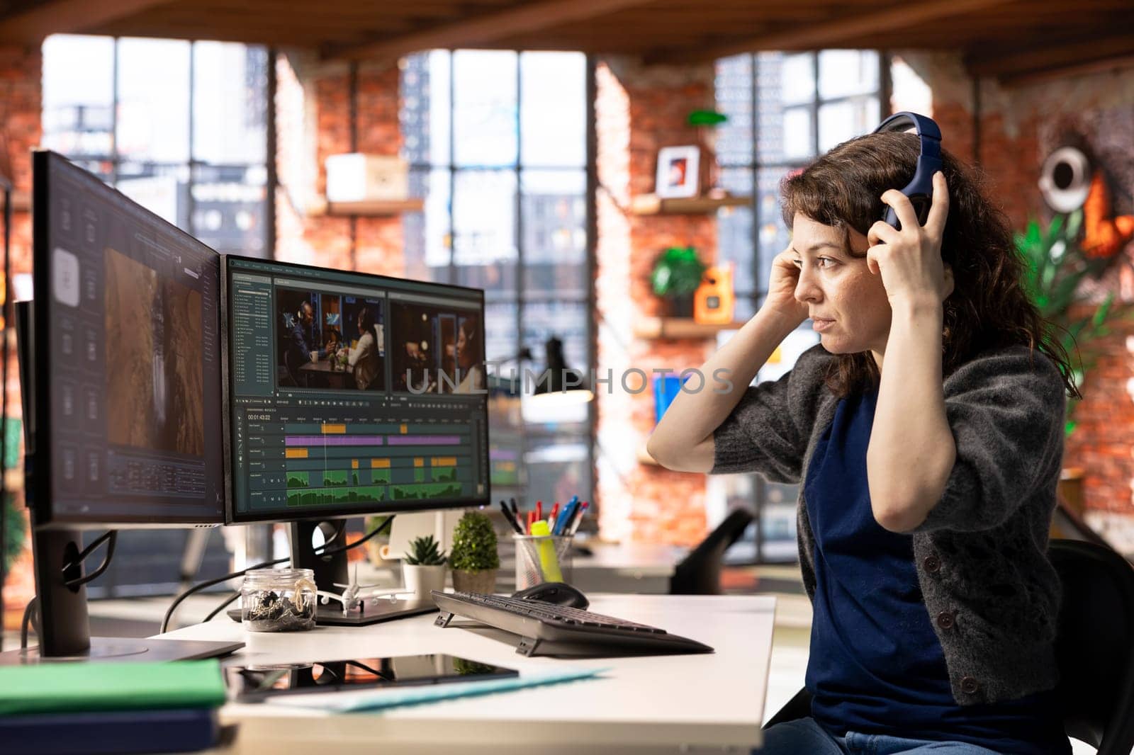 Woman filmmaker editing video footage with professional software, creating a montage for a cinematic project using dual monitors at the agency. Editor working on a creative process.