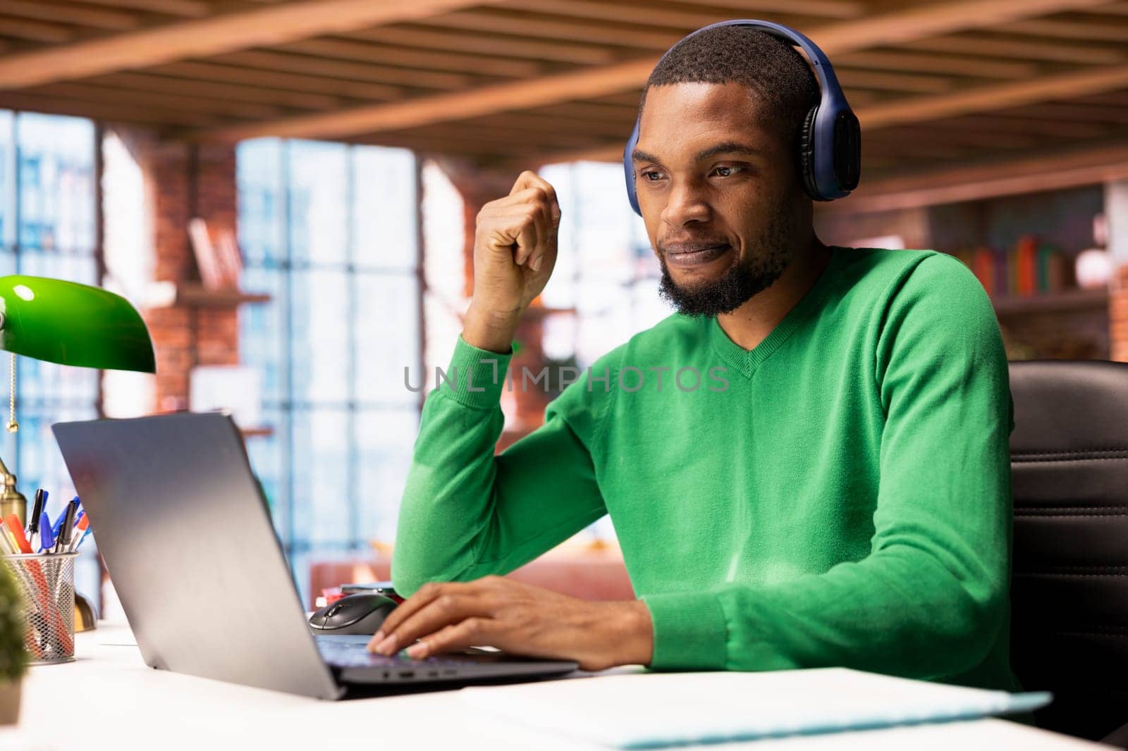 Remote employee wearing headphones at home participating in online training session on laptop. Teleworker using audio device at home to watch instructional course videos on notebook