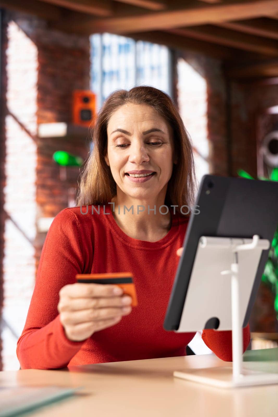 Smiling woman entering her credit card digits to confirm a money transfer, setting up the payment for online shopping on her tablet. Happy woman feeling good after placing orders in her loft.