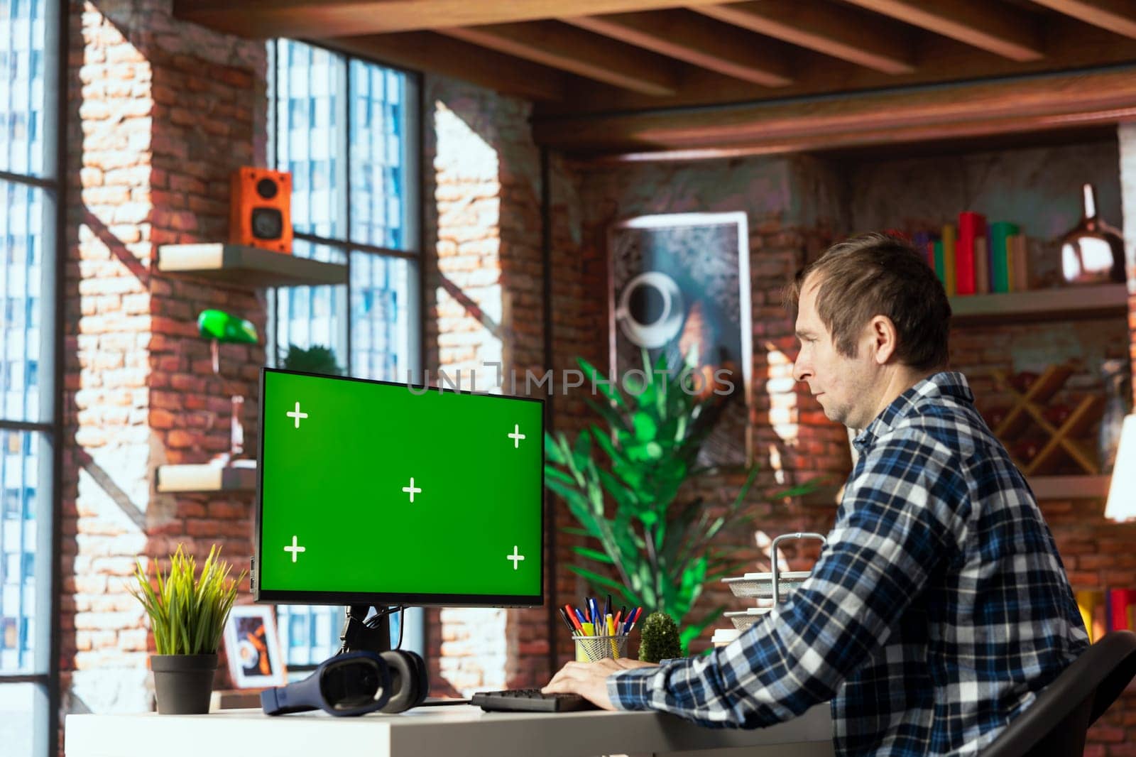 Person at home office desk browsing internet on green screen computer monitor, researching information online. Man coding software at workspace desk, writing and testing program code on chroma key PC