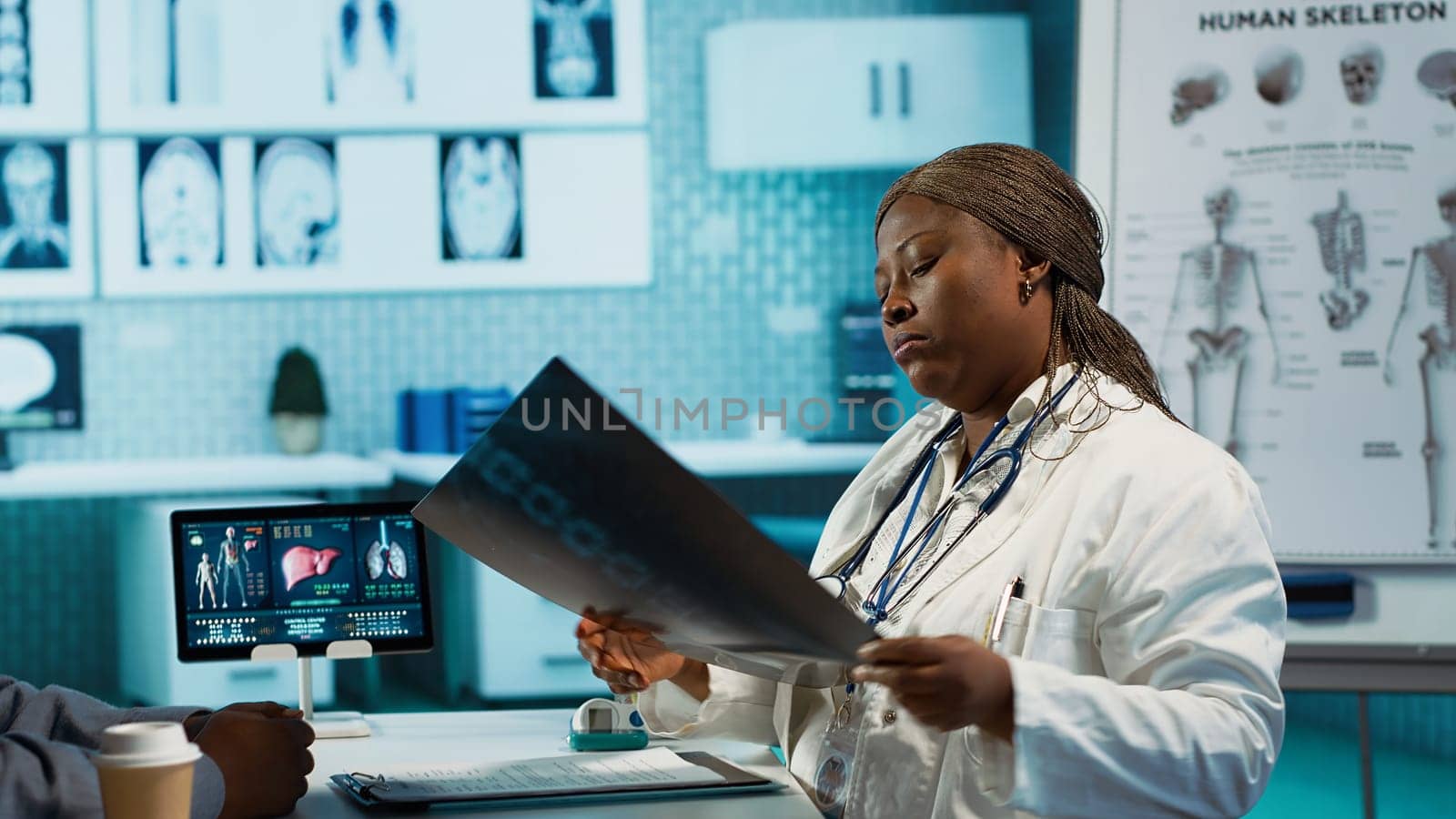 General practitioner reviewing x ray imaging at checkup with male patient, offering her professional expertise to ensure wellness. Medic doing scan interpretation with a man in the office. Camera A.