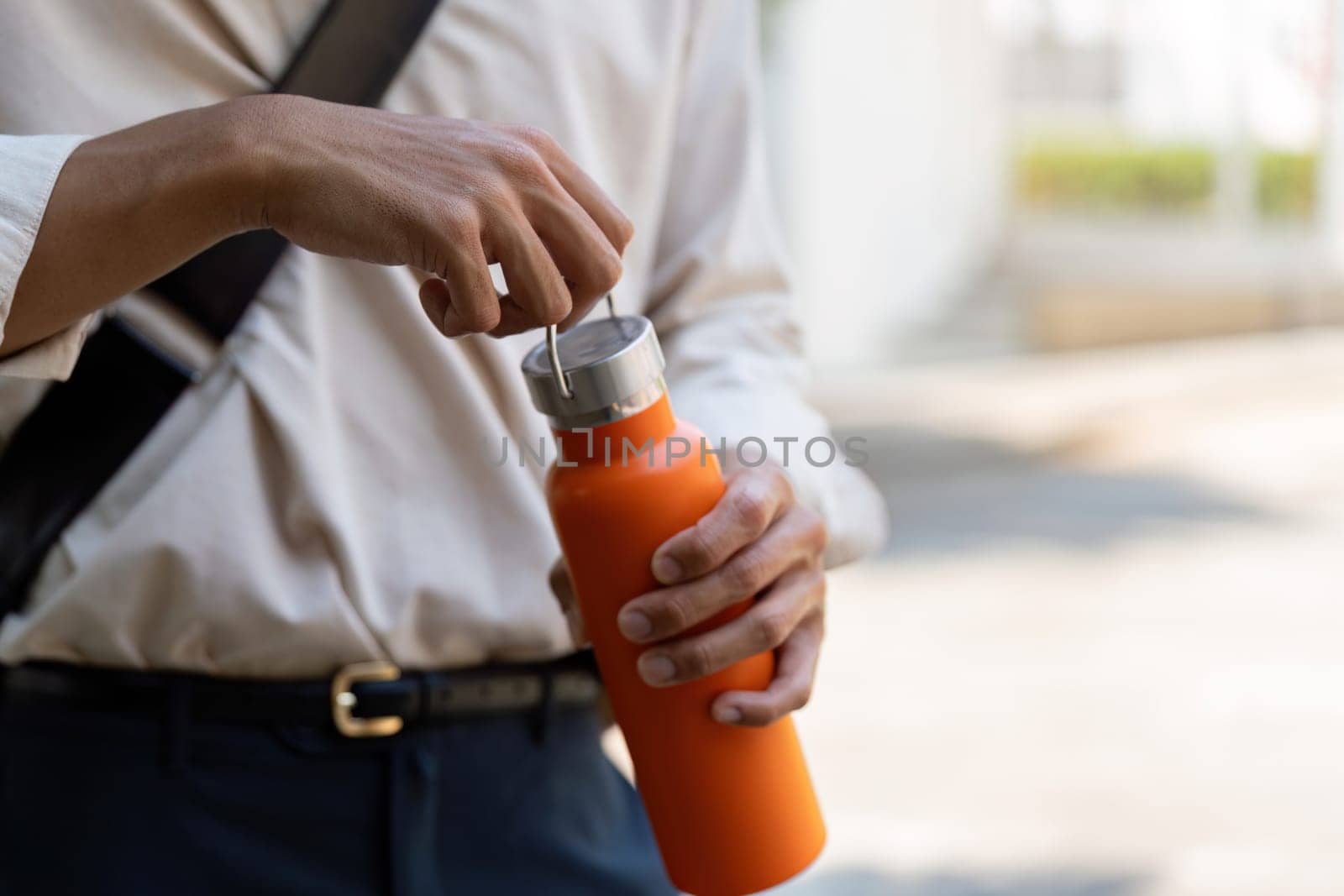 A man is seen opening his orange reusable water bottle, showcasing sustainable hydration choices while minimizing plastic waste.