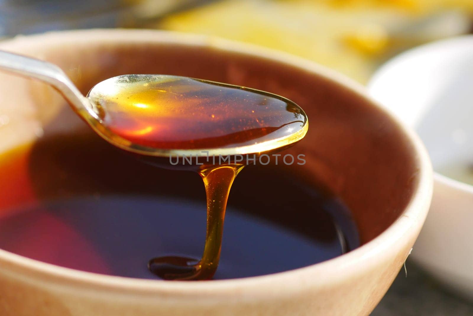 Golden honey flows from a spoon into a clay bowl on a sunny day.