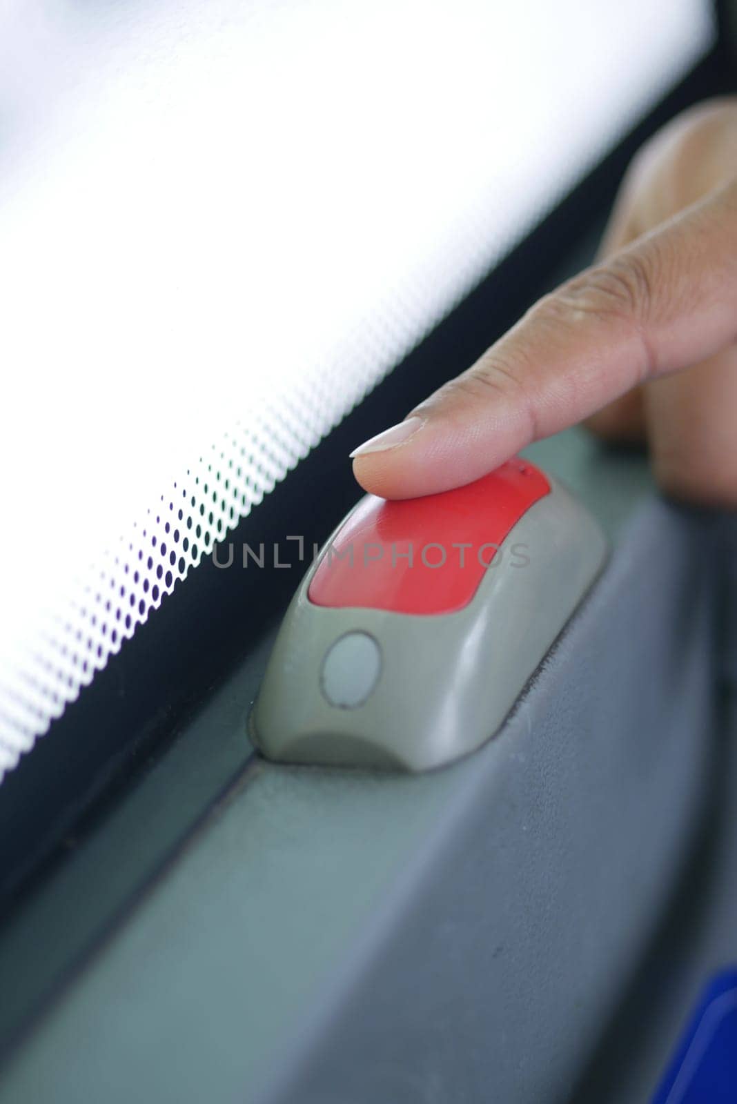 A hand gently presses the stop button inside a bus.