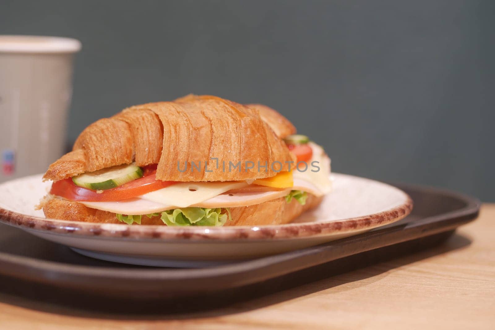 A croissant sandwich with veggies and cheese sits on a plate, invitingly.