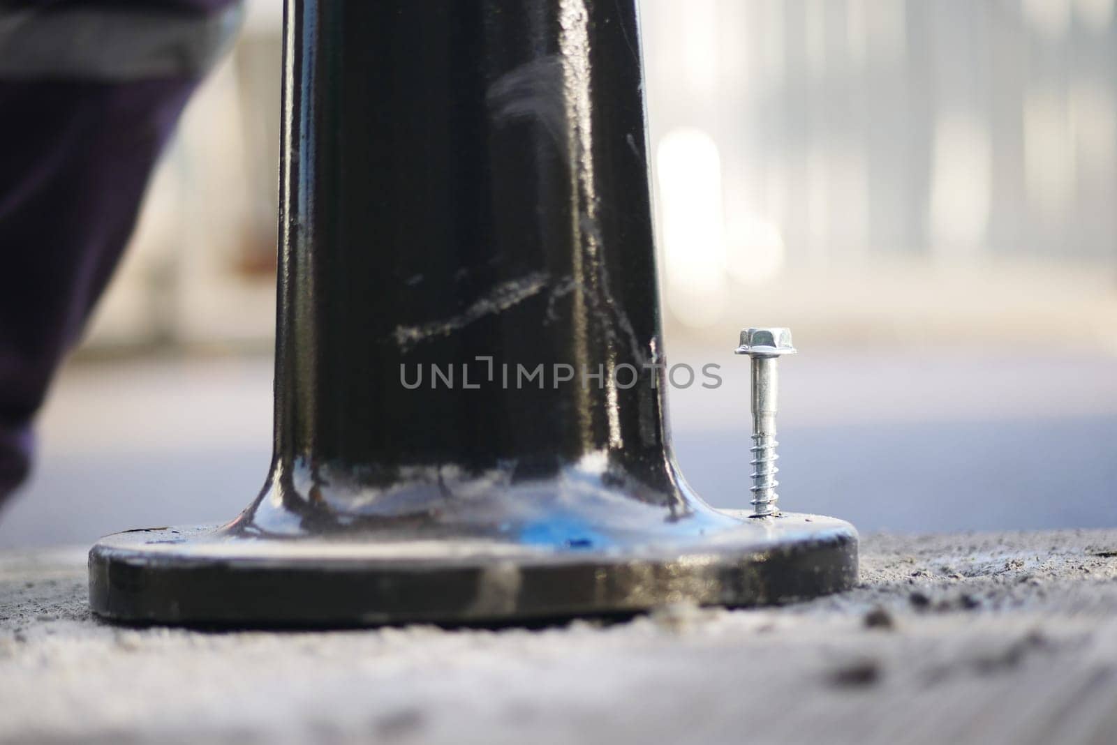 A person repairs the base of a pole with a screw on the pavement.