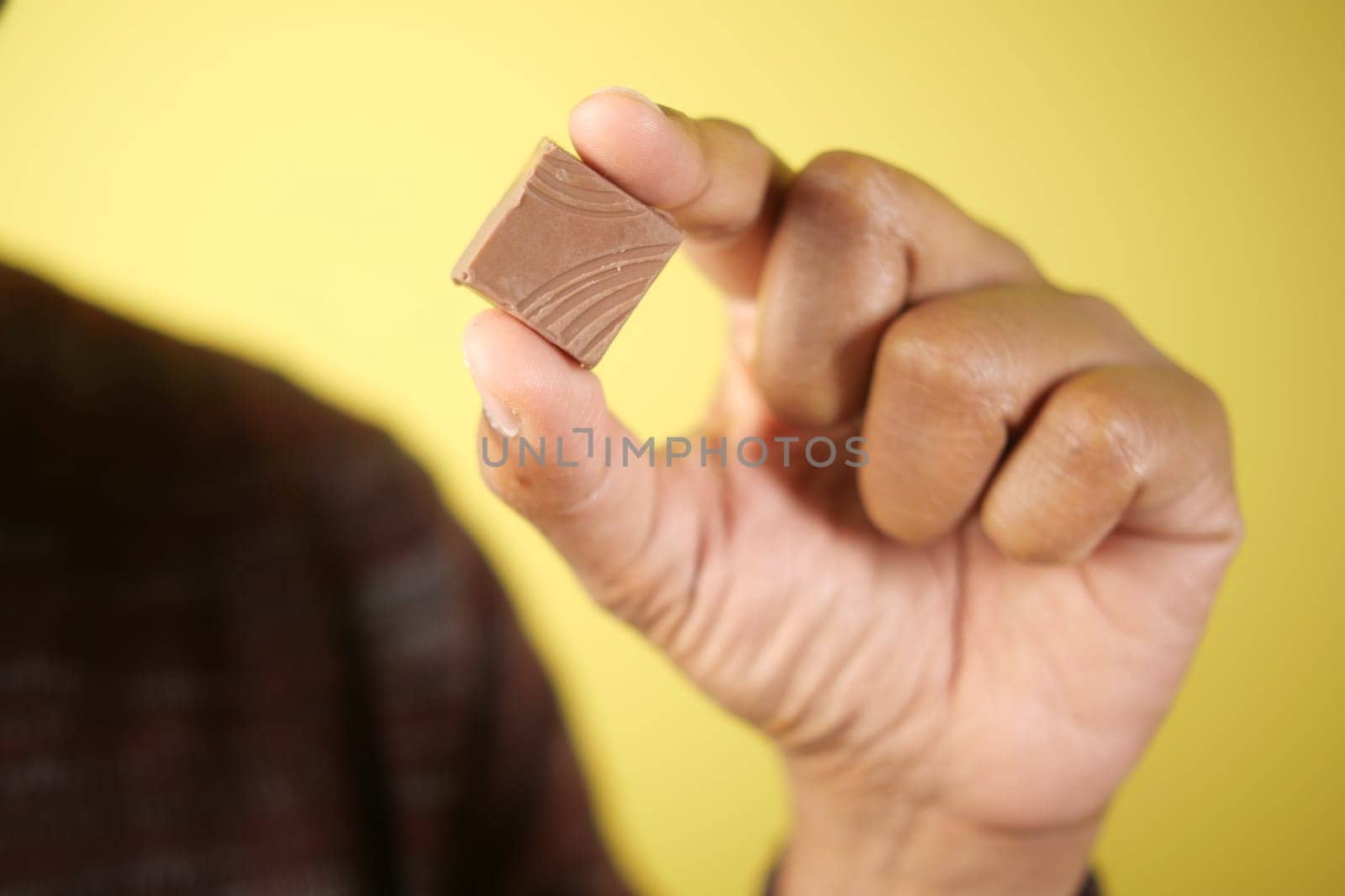 Person presents a small chocolate piece with a vibrant backdrop.