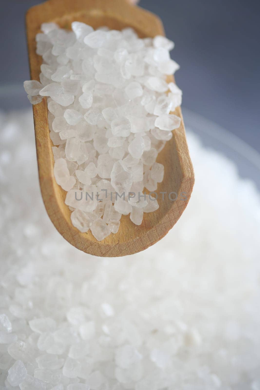 A wooden spoon lifts coarse sea salt from a bowl, highlighting its texture.
