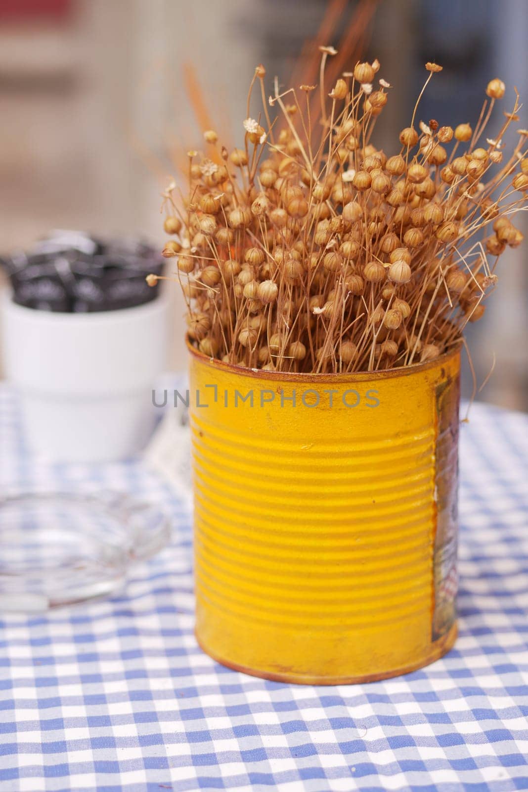 Dried flowers are arranged in a yellow tin on a checkered table.