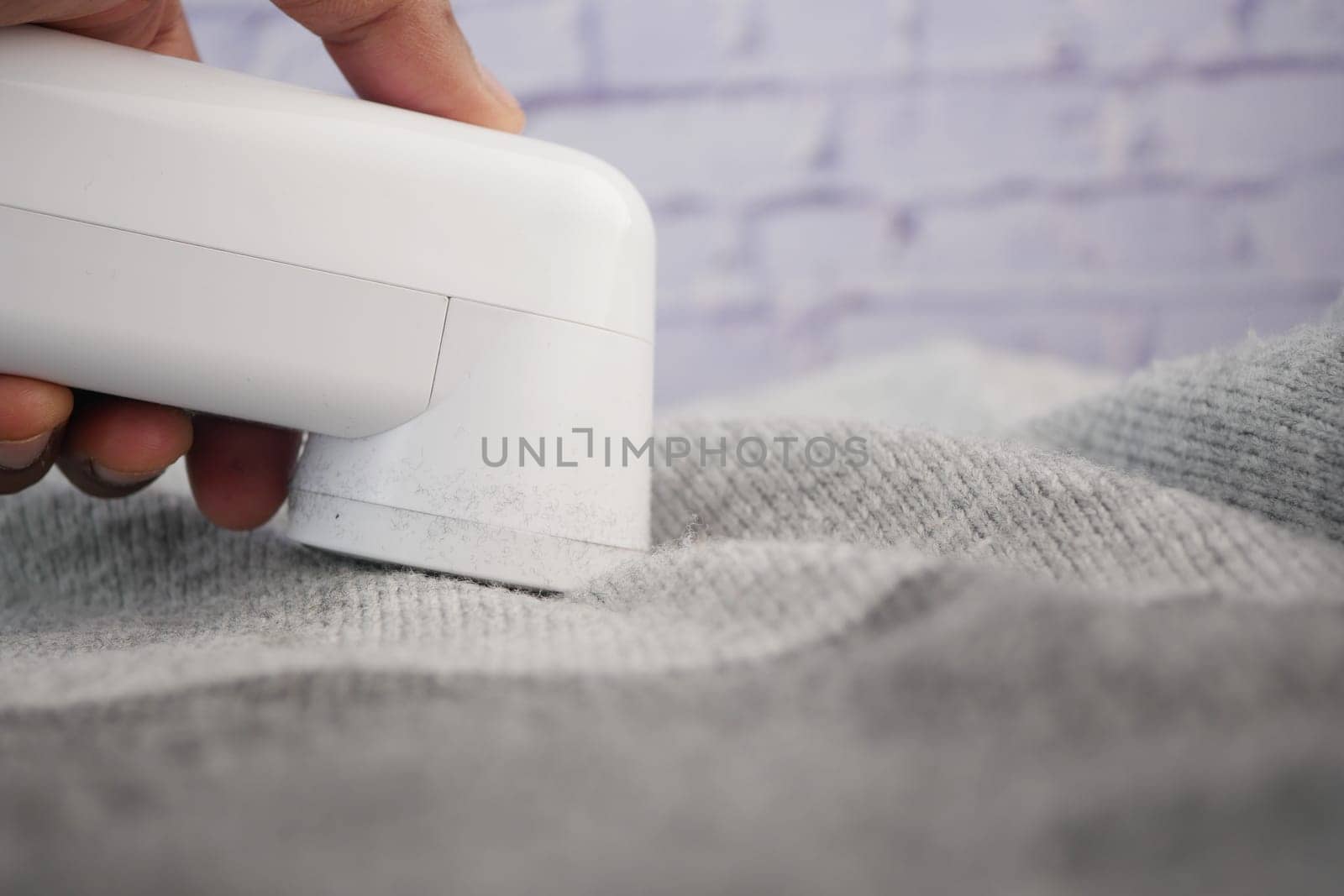 Person using a lint remover on grey fabric to clean it from lint.