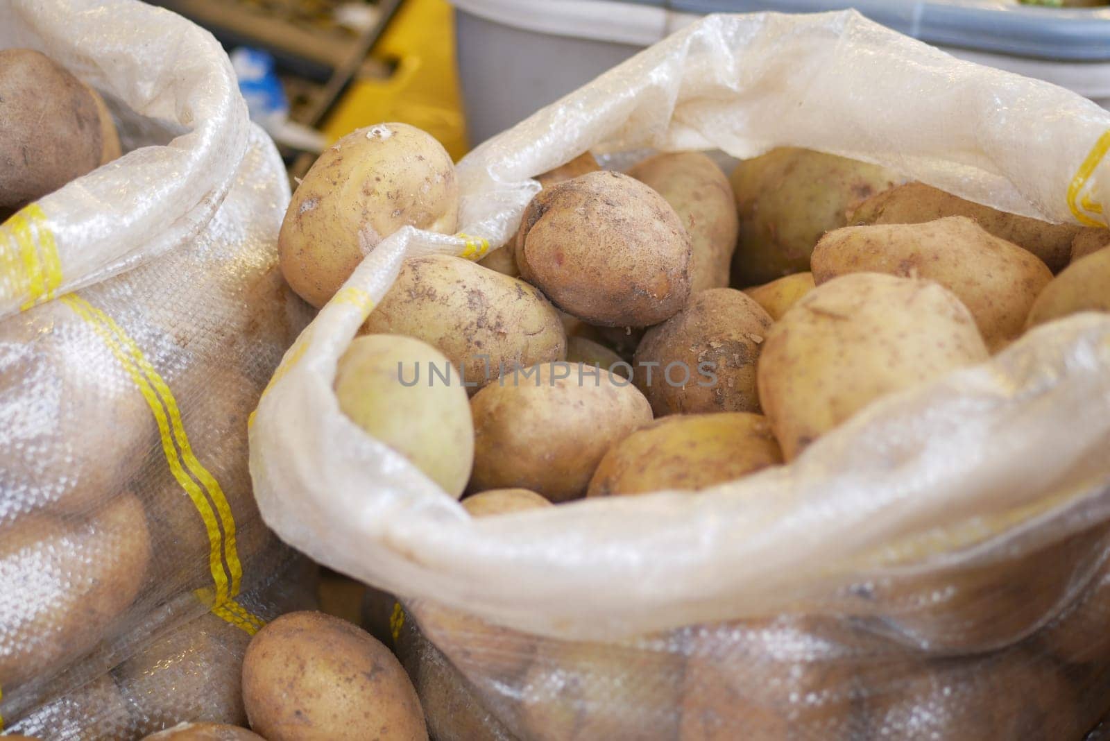 Vendors display fresh potatoes in mesh bags at a bustling market.