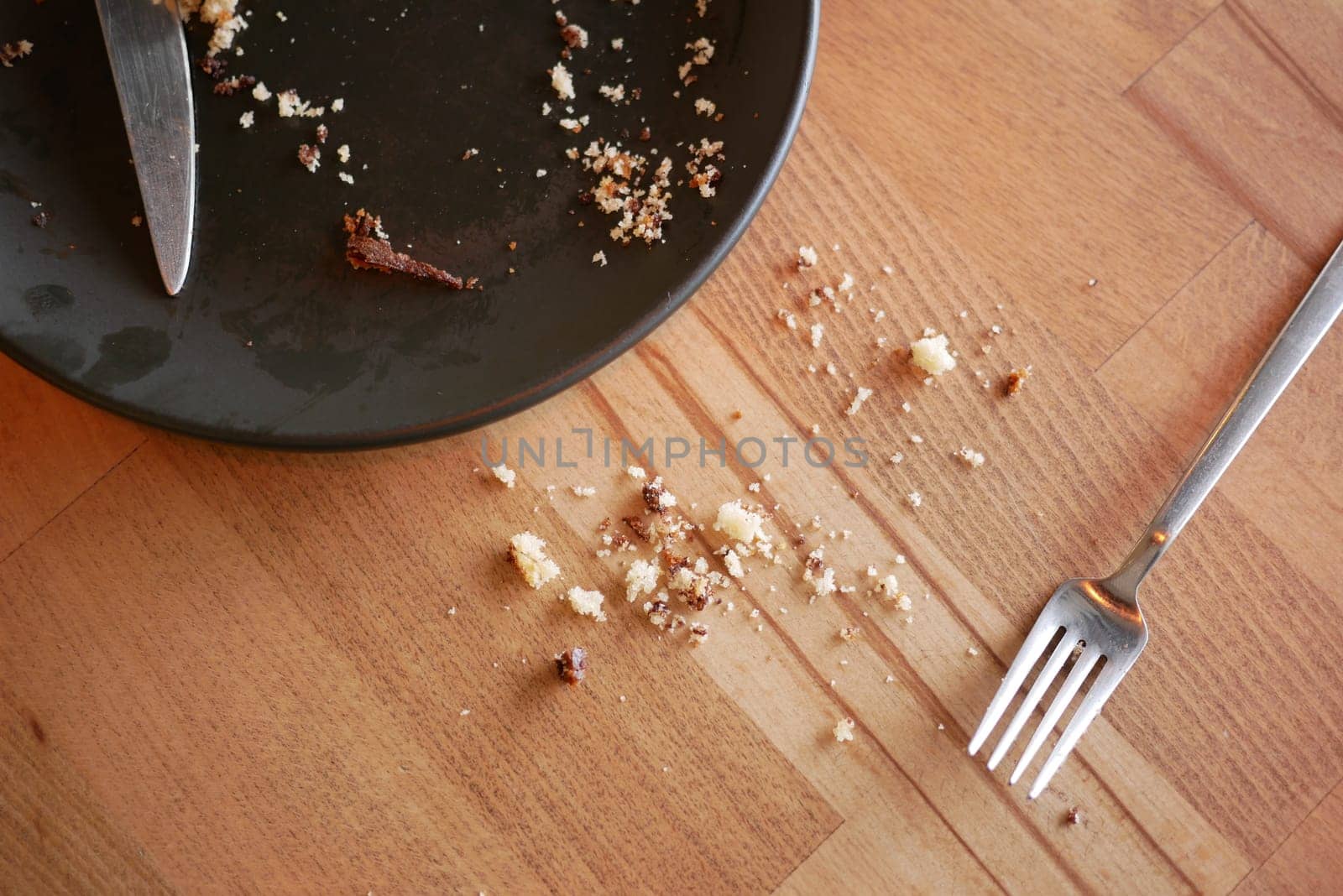 Leftover crumbs and utensils linger on a wooden table after dining.