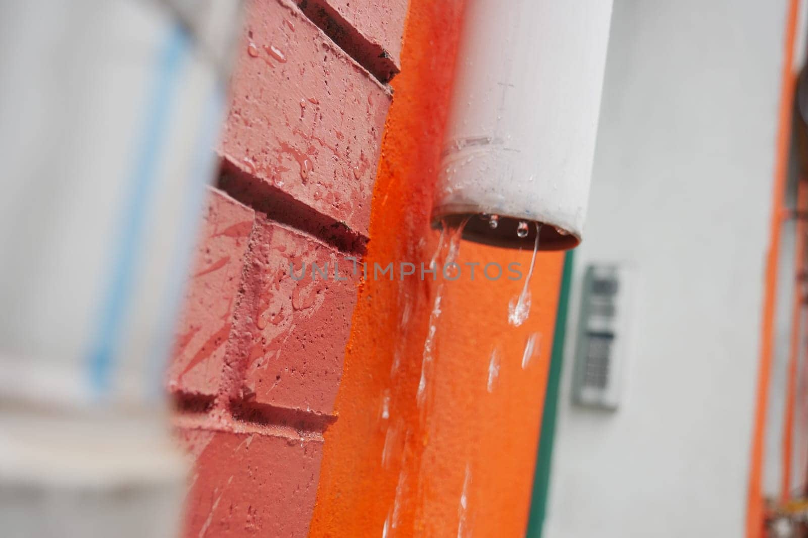 Water cascades from a rain gutter against a vibrant wall.