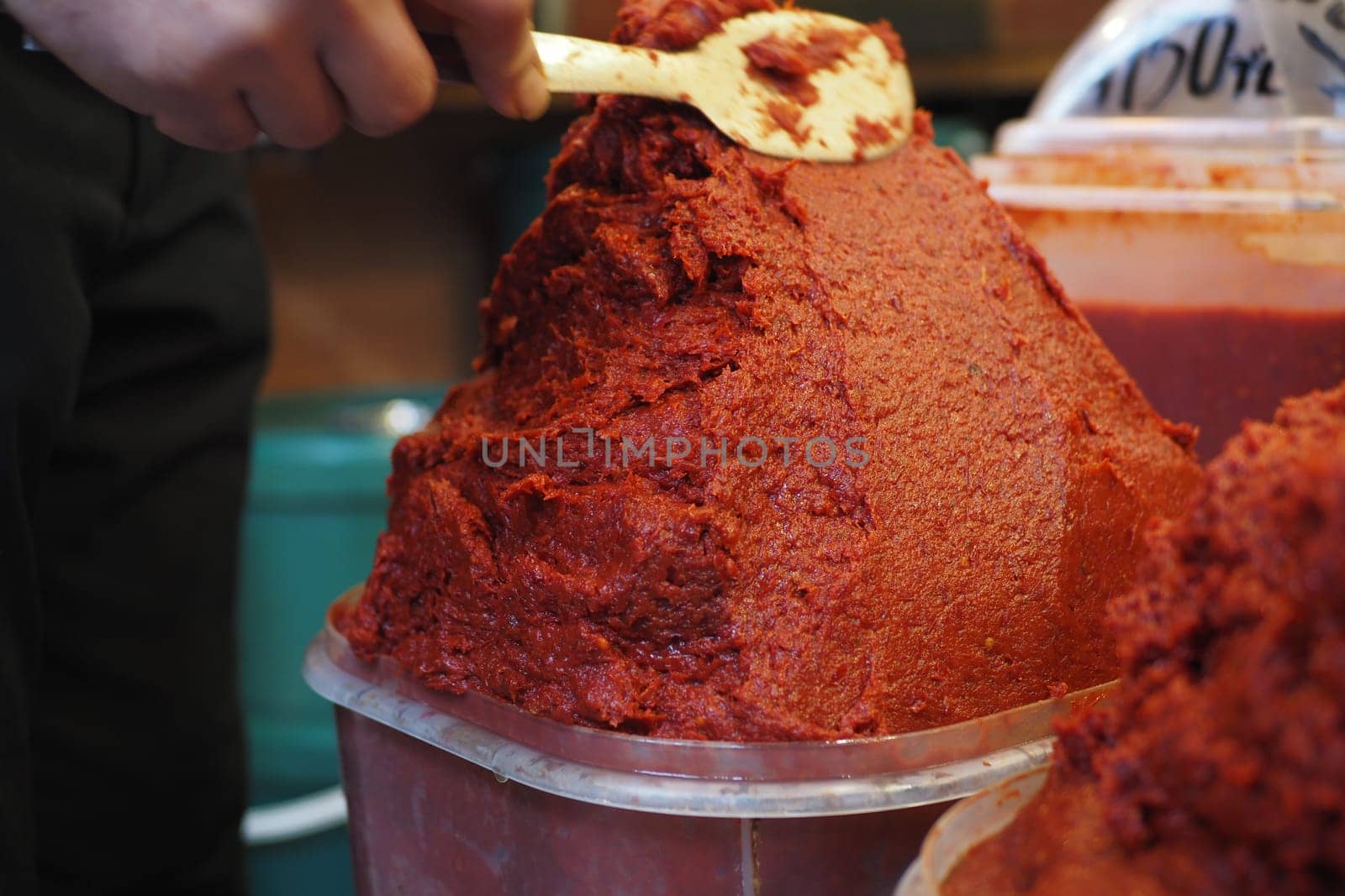 A vendor prepares vibrant red pepper paste in a bustling market.
