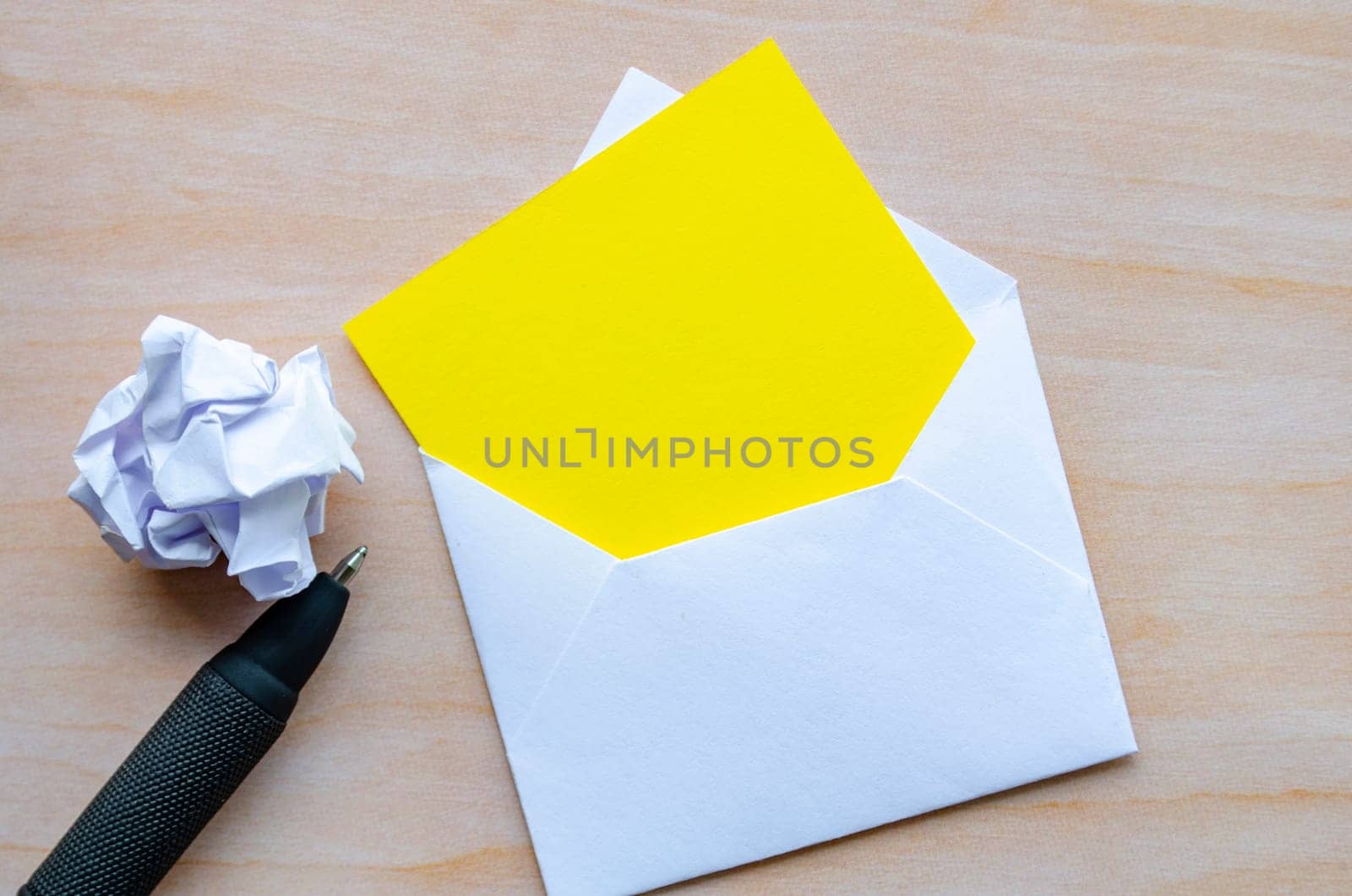Top view of empty yellow notepad inside an envelope with crumpled paper and pen with customizable space for text.
